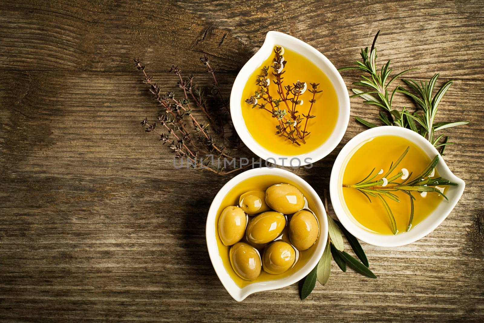 Olive oil with fresh herbs on wooden background.