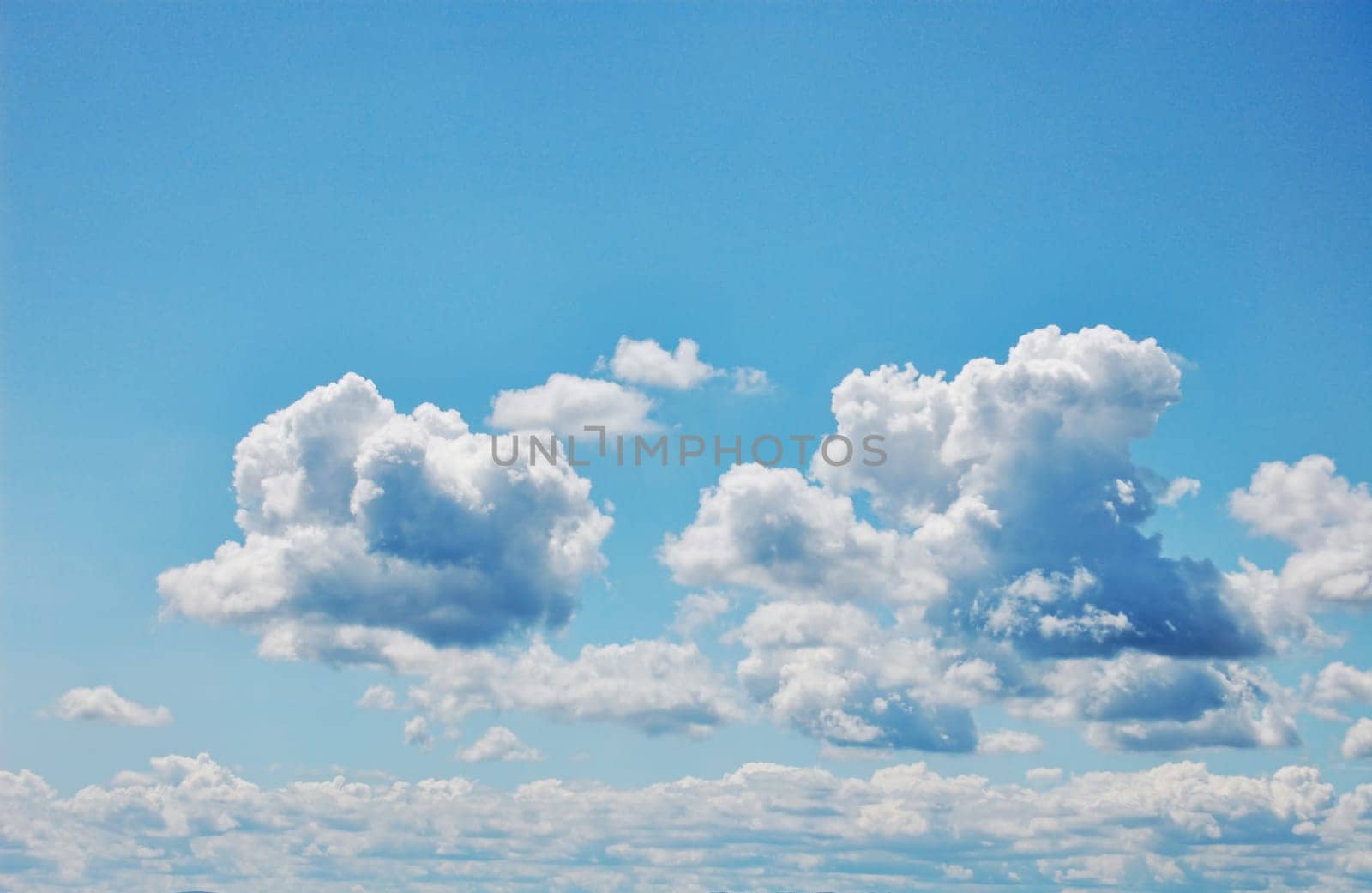 Blue sky with fluffy white clouds. Wide format. Photographic Image.