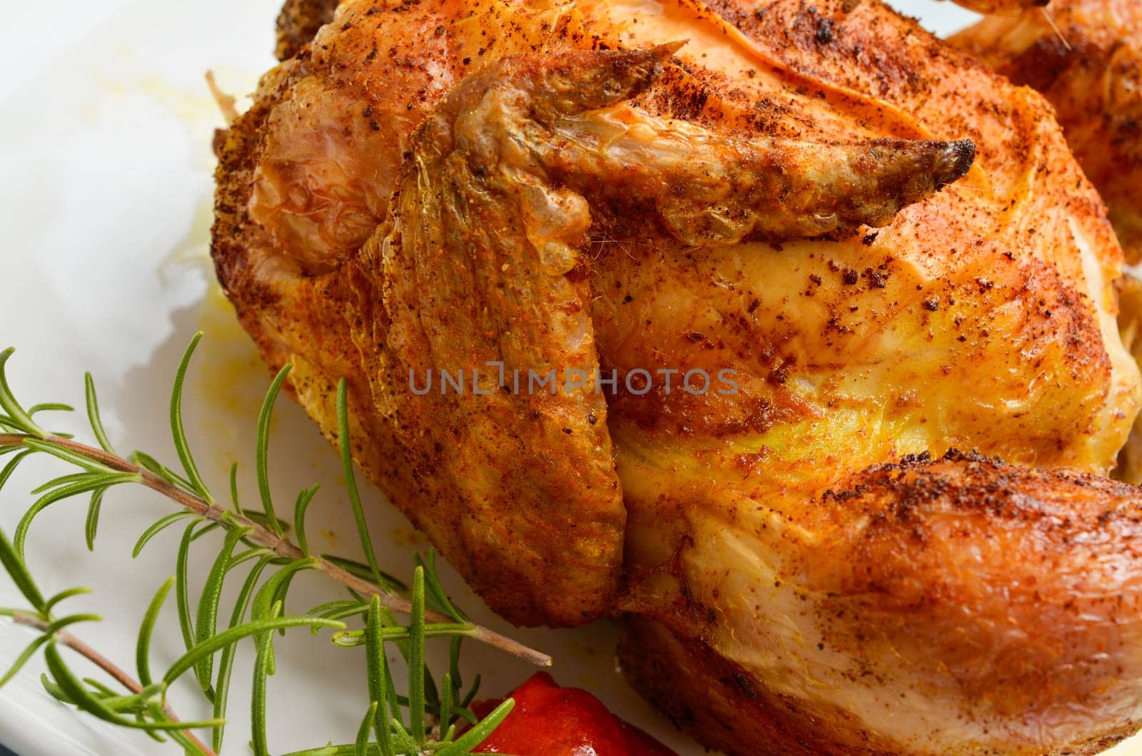 Roasted chicken on a white plate with a twig of rosemary