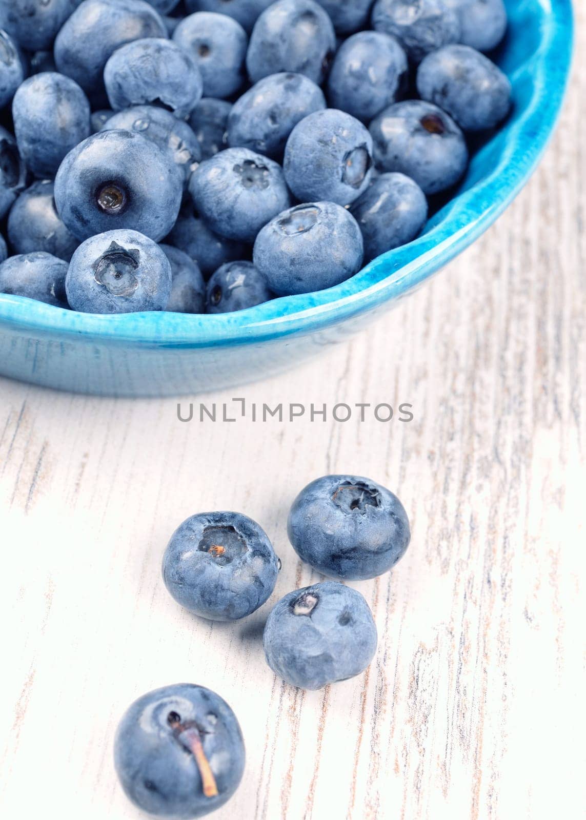 Fresh blueberries in a rustic blue bowl on a wooden table toned in vintage colors