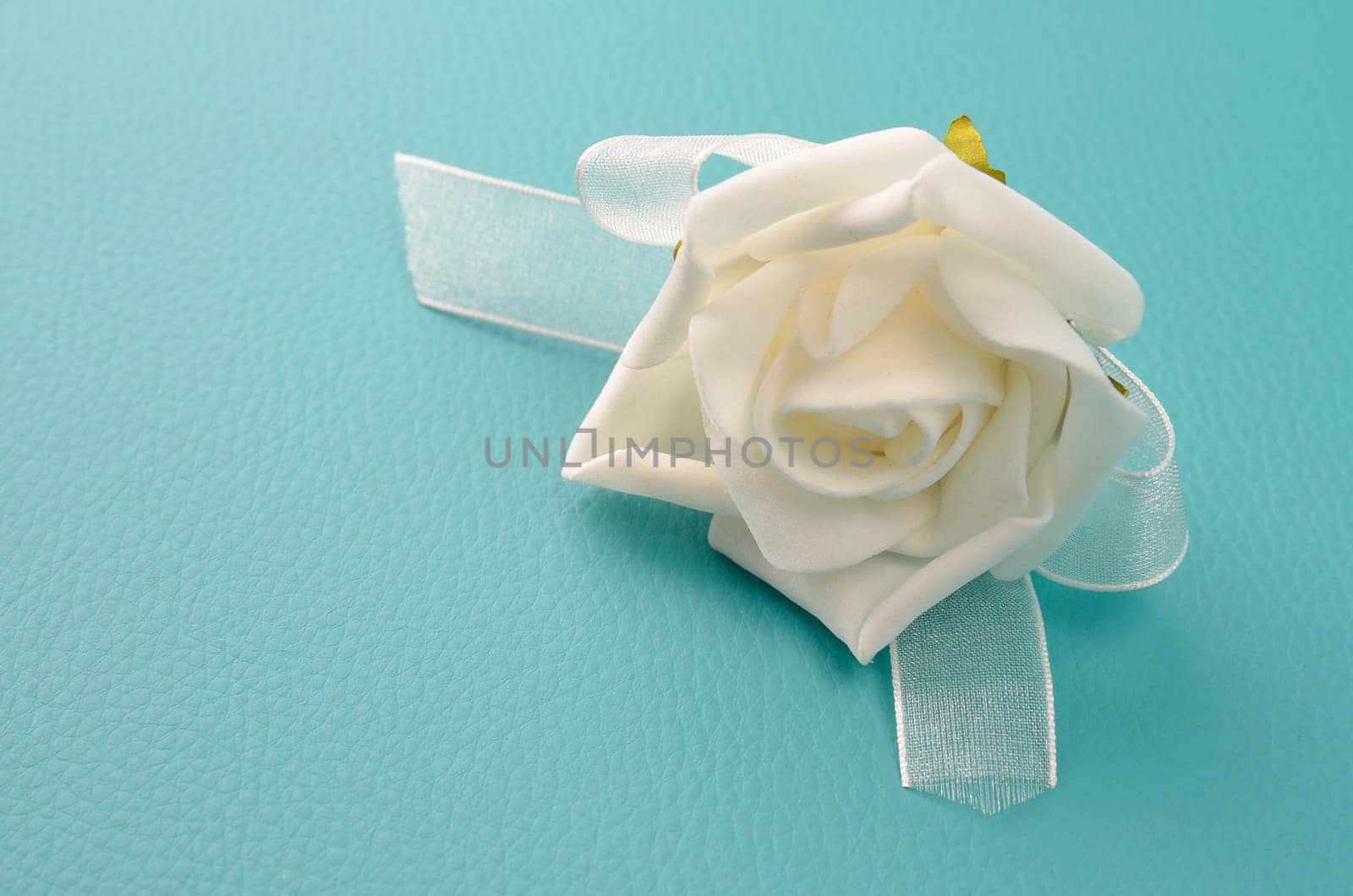 White plasic foam rose on a turquoise leather background with space for text