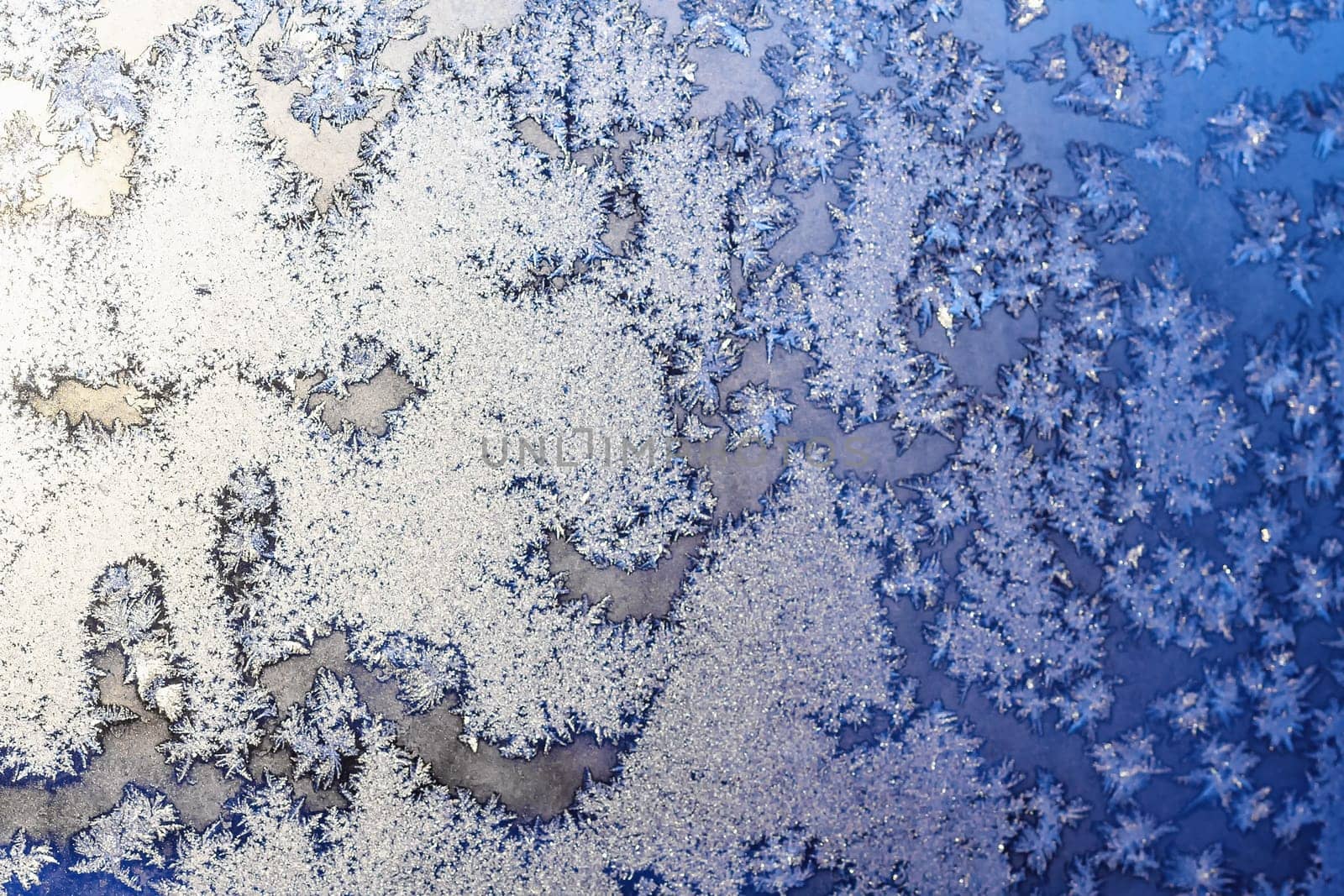 Ice snowflakes and frost pattern on Christmas winter frozen window. Blue color background. Selective focus with blur edges of image