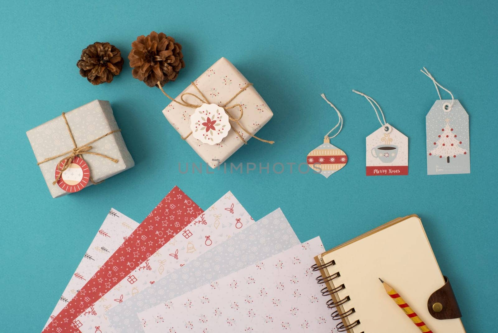 Christmas stationery arrangement of elements top view template. Empty spiral notebook with wrapping paper stack, vintage gift boxes and holiday decoration.