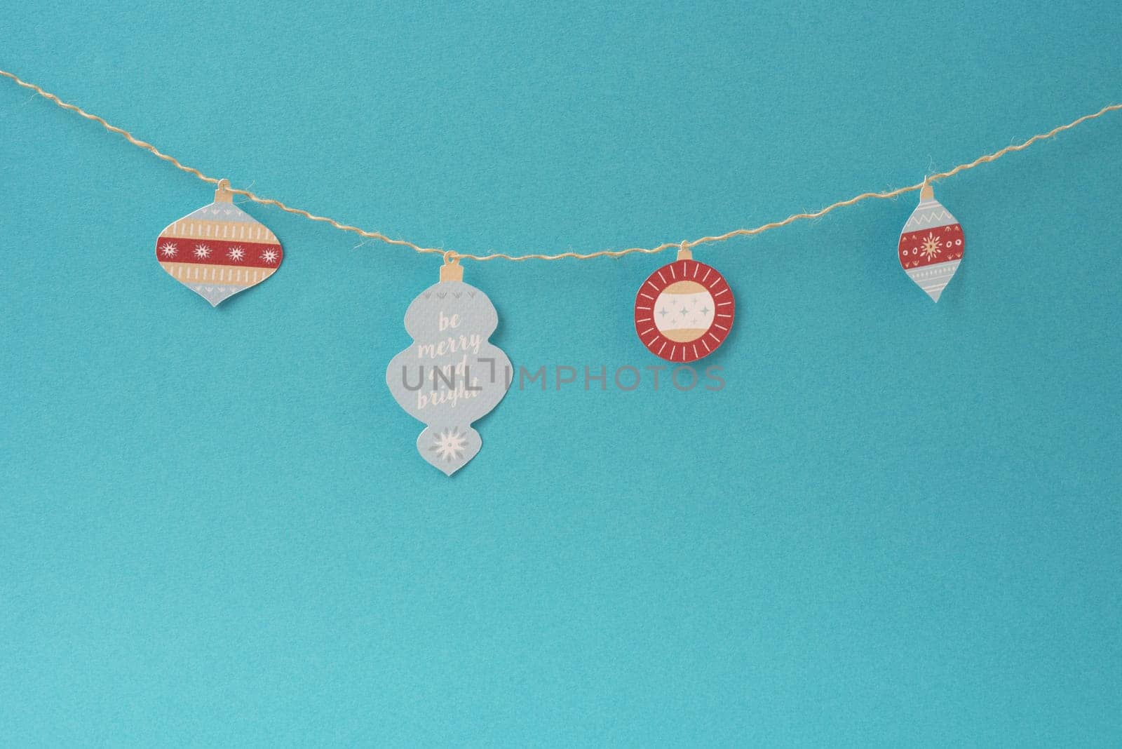 Christmas paper decoration, simple handmade Xmas label ornaments hanging on string over empty blue background with blank space.