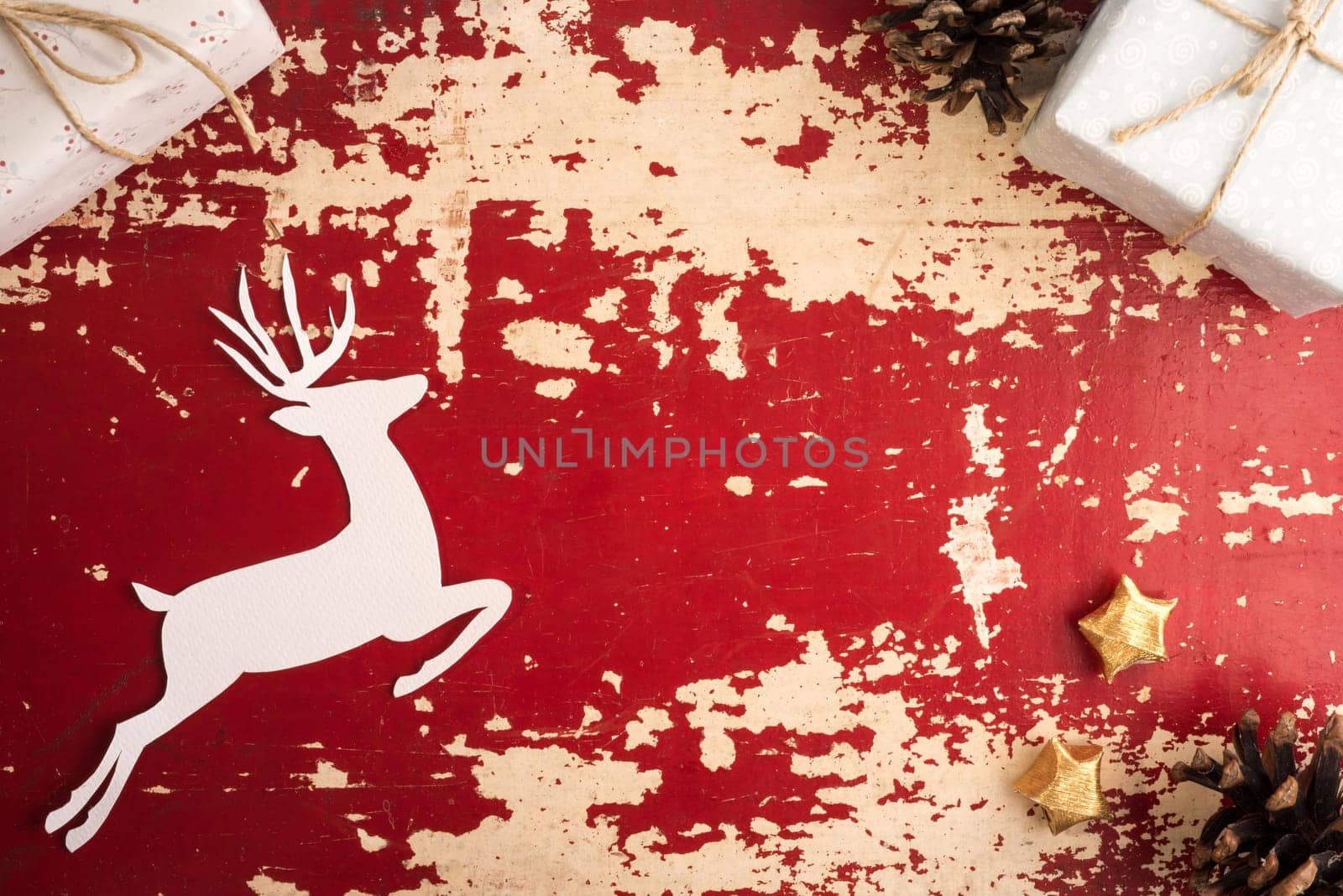 Vintage christmas time top view concept scene with copy space. Retro holiday decoration and paper cut reindeer silhouette on red grunge wood background.