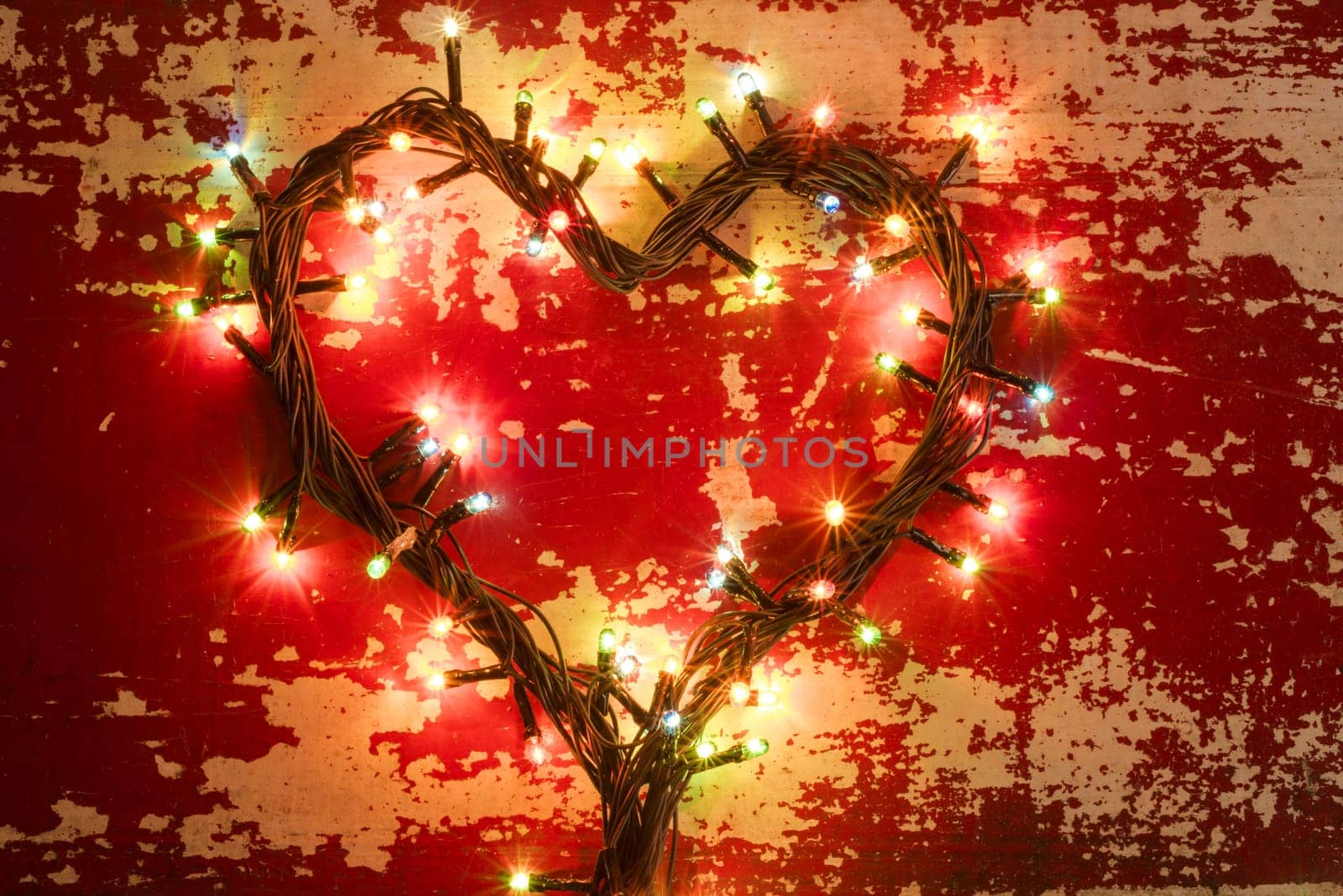 Holiday concept, love composition with heart shape made from christmas lights on grunge wood texture background.
