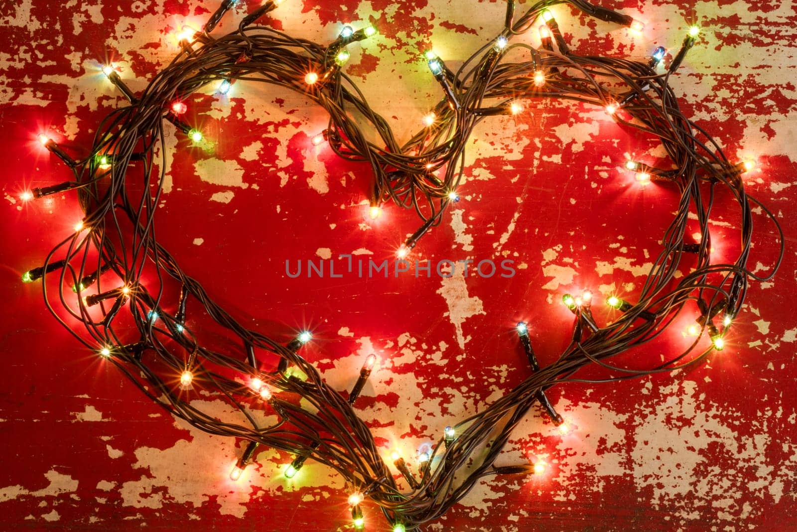 Holiday greeting card love concept background, heart shape made with christmas lights on grunge wood texture.