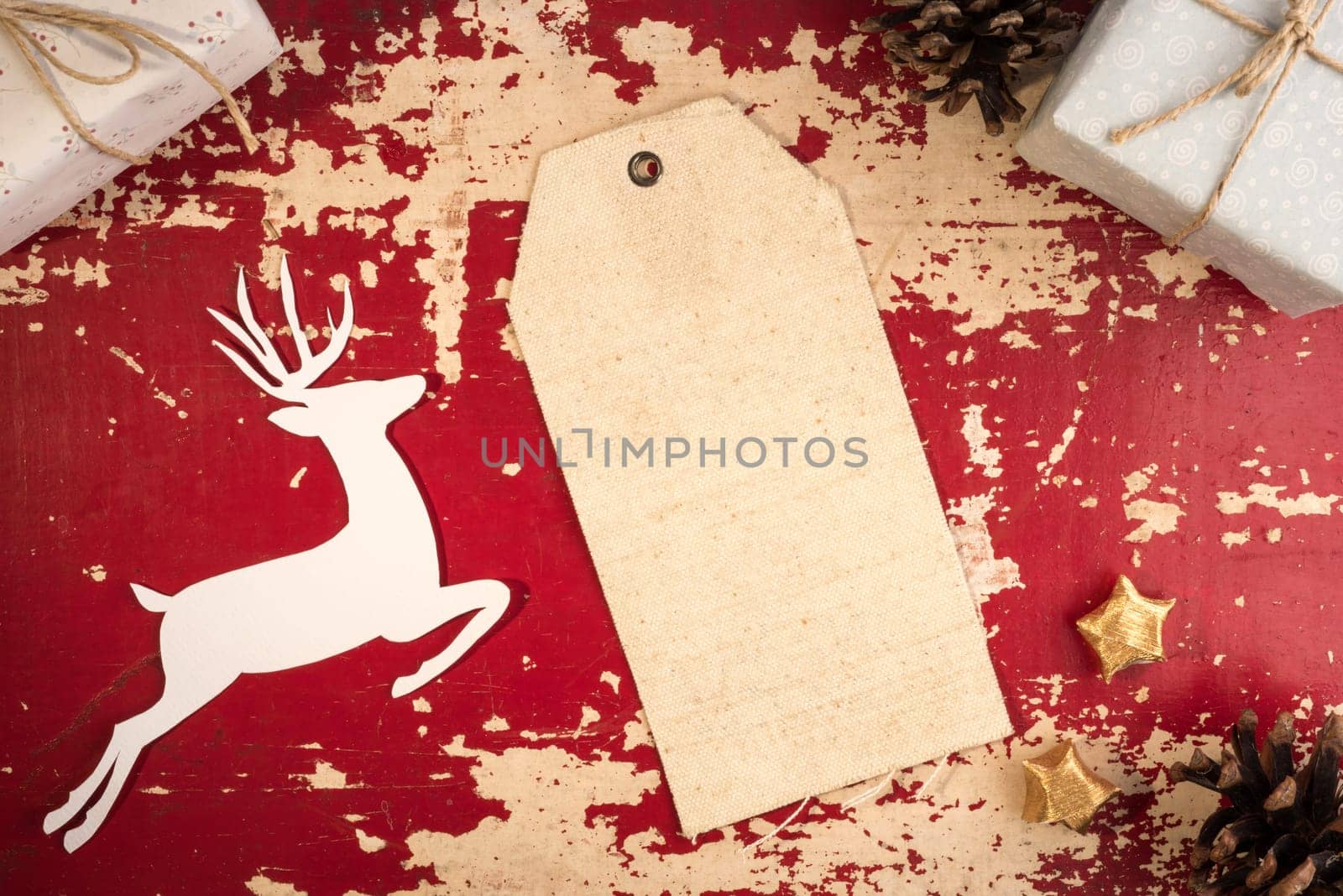 Merry Christmas top view vintage fabric hang tag label template with paper cut deer silhouette and holiday decoration elements on red vintage grunge wood background. Includes clipping path.