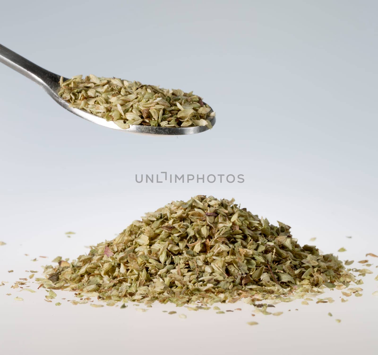 Dried oregano on Tablespoon with a pile beneath it.