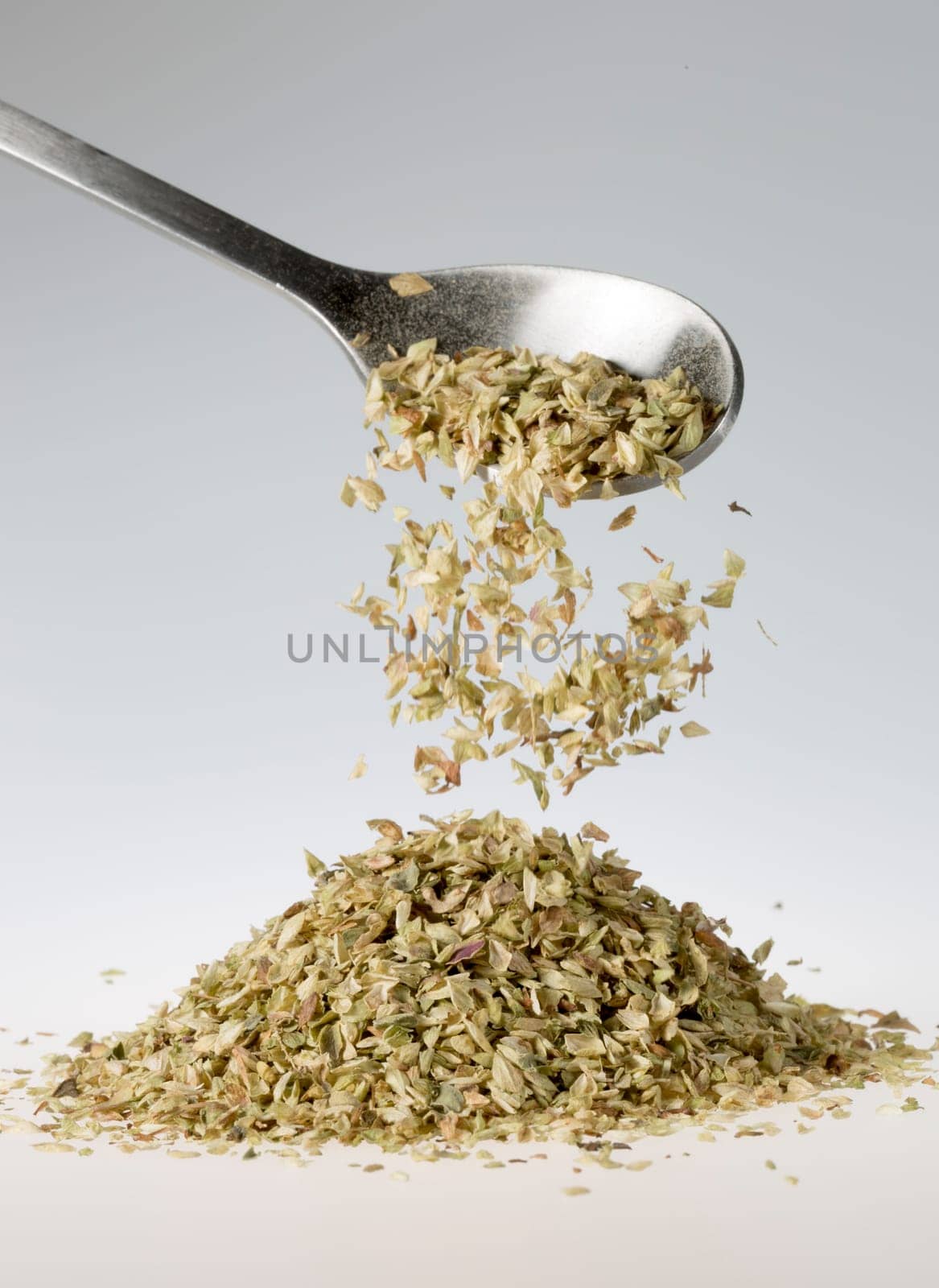 Dried Oregano Falling from Tablespoon onto pile beneath it.
