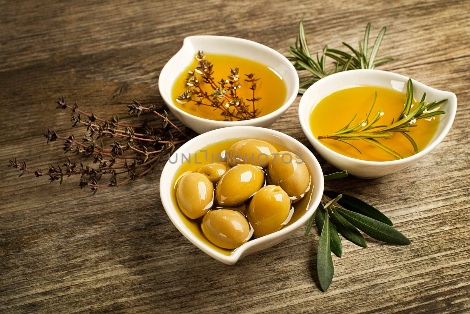 Olive oil with fresh herbs on wooden background.