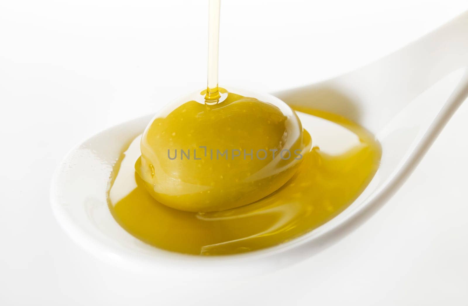 Virgin olive oil pouring on white spoon.