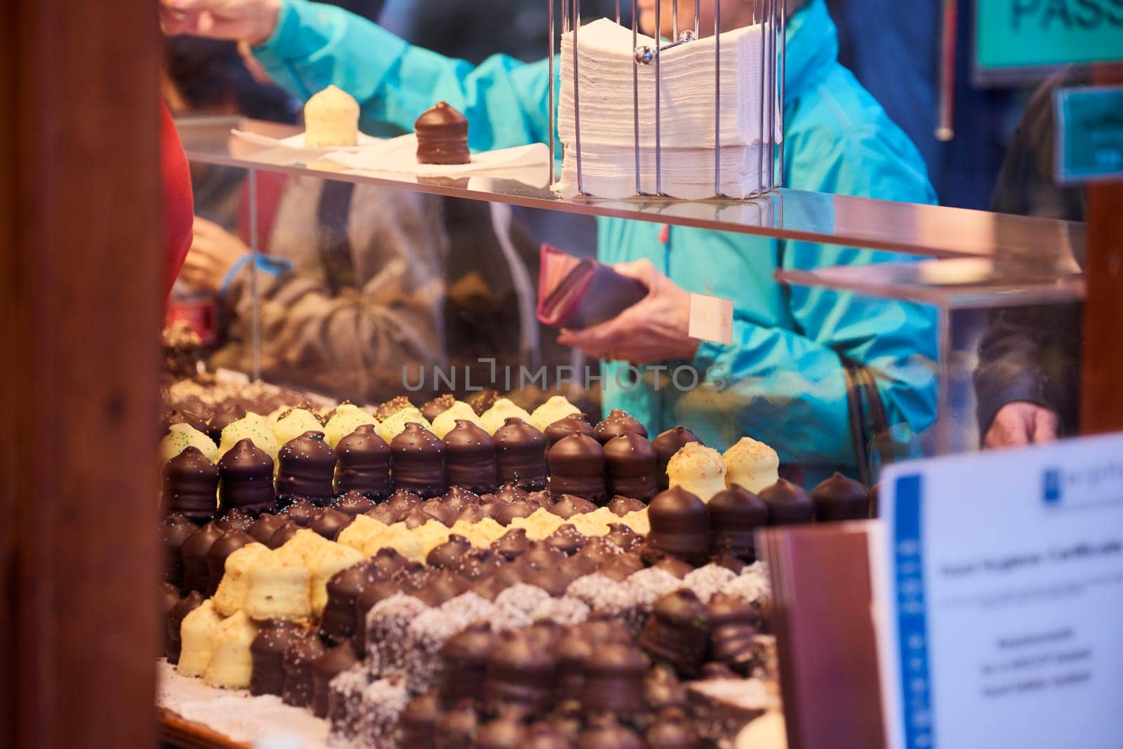 Cropped shot of chocolate covered marshmallow snowballs with consumer paying over the counter in the background.