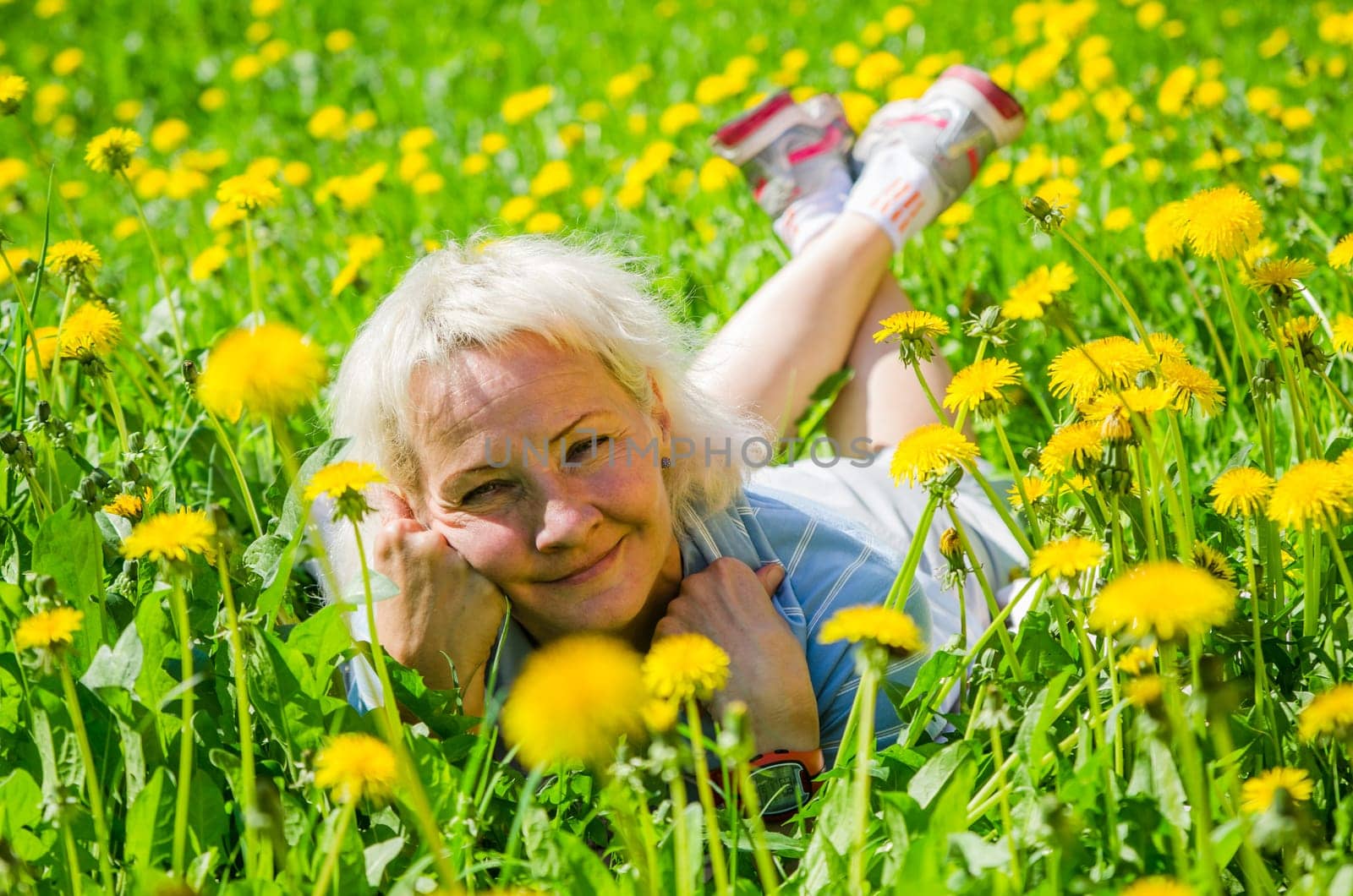 A woman lies in a clearing among the dandelions and sniffs a flower