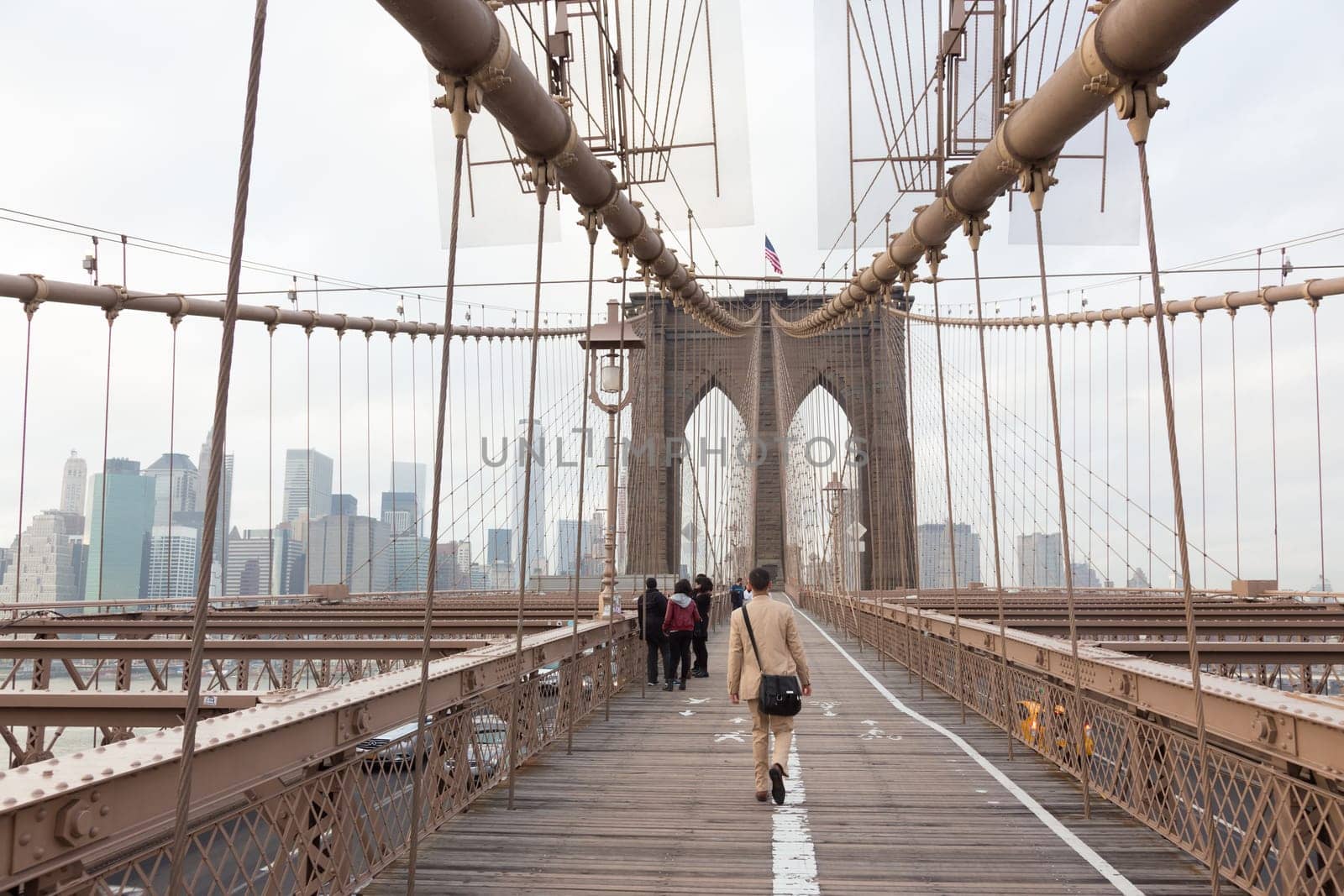 Man walking on pedestrian path across Brooklyn bridge. New York City Manhattan downtown with skyscrapers over East River panorama as seen from Brooklyn bridge.