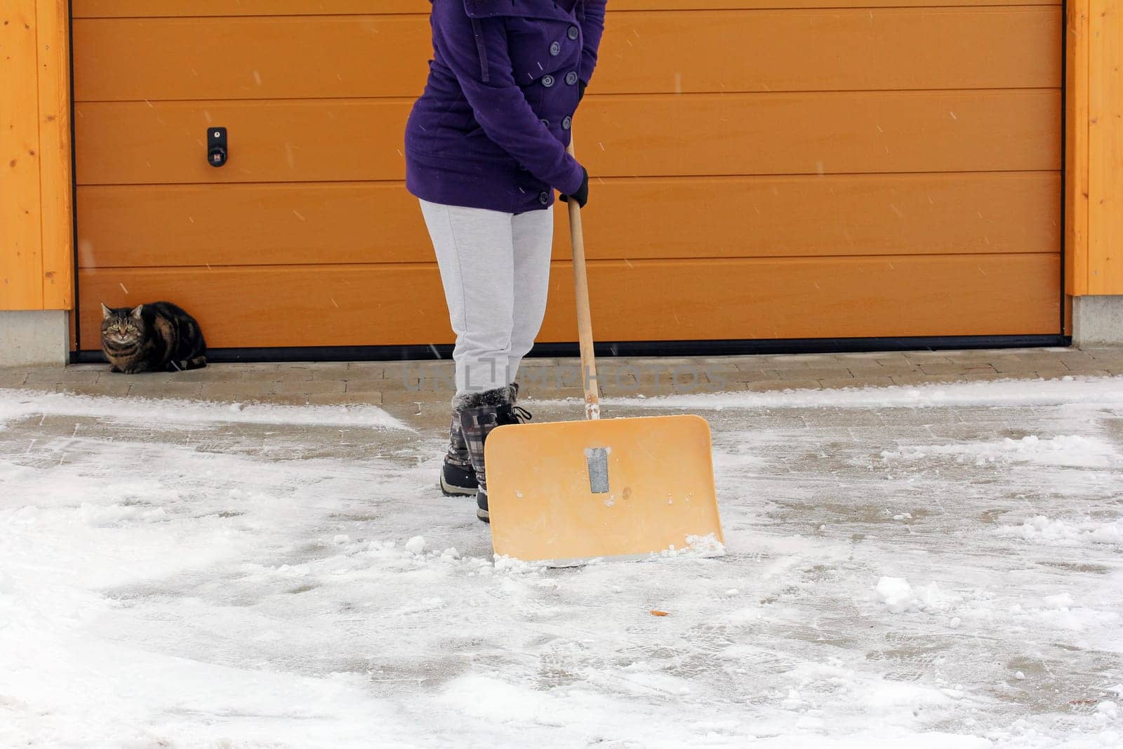 Snow clearing in winter - A woman clears snow in front of a garage