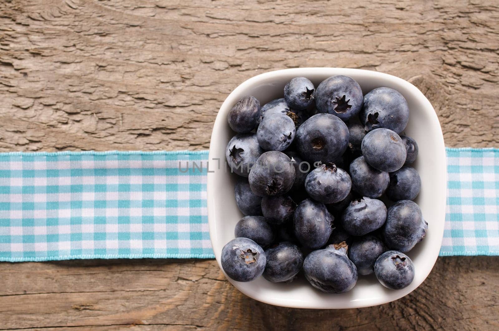 Fresh blueberries in a white bowl on an old table, top view