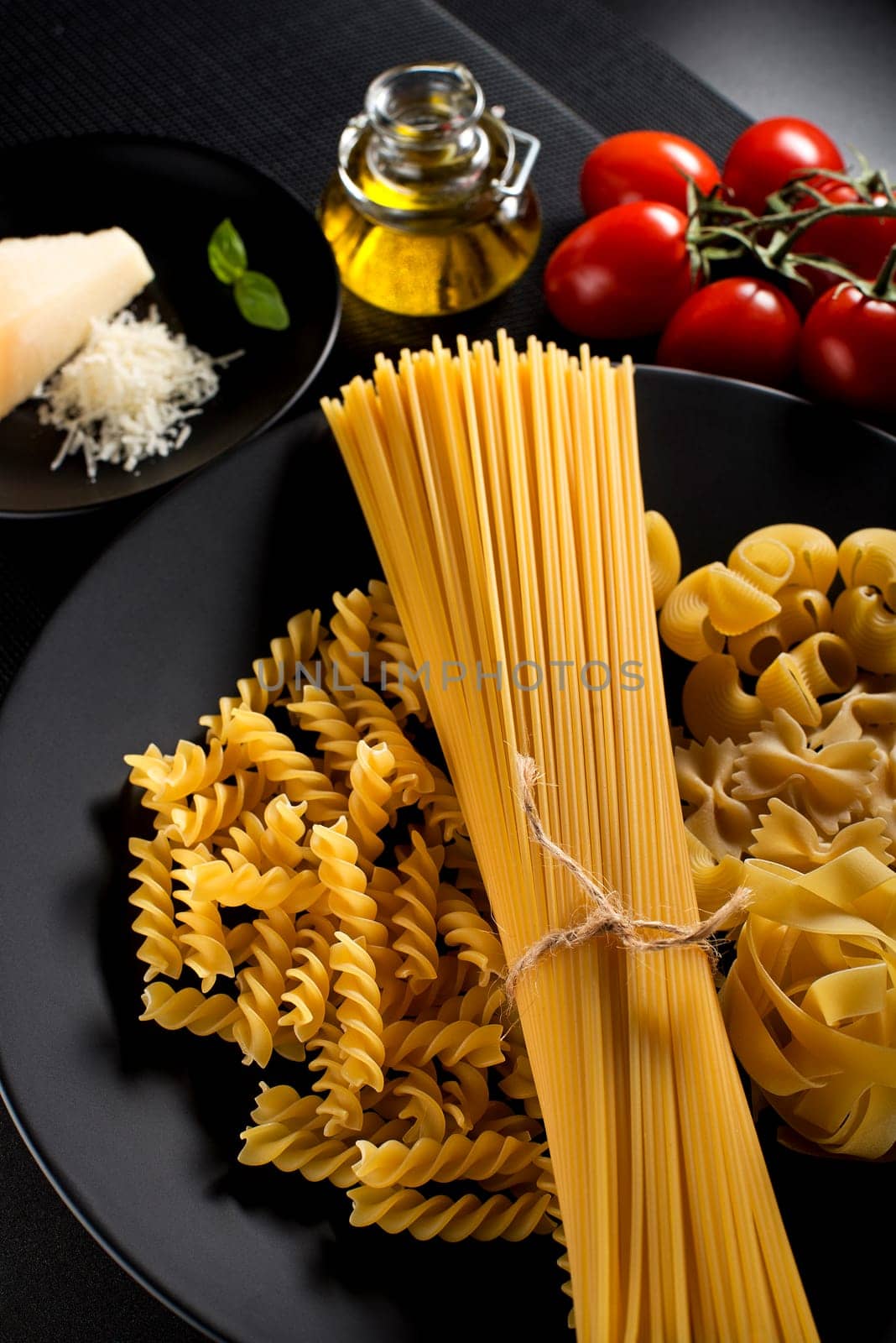 Raw mixed pasta with ingredients on black background.