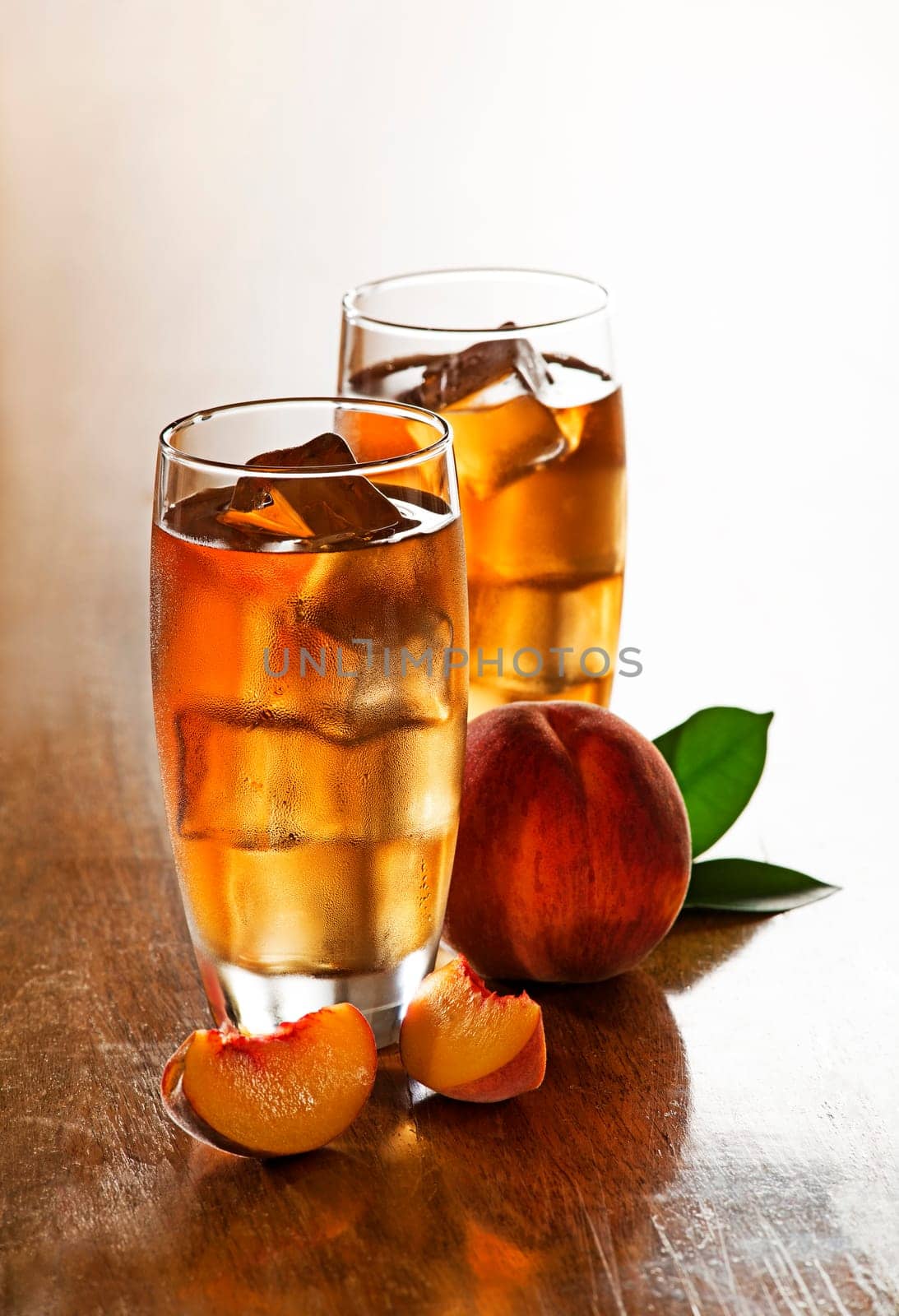 Glass of peach ice tea with slices cubes.