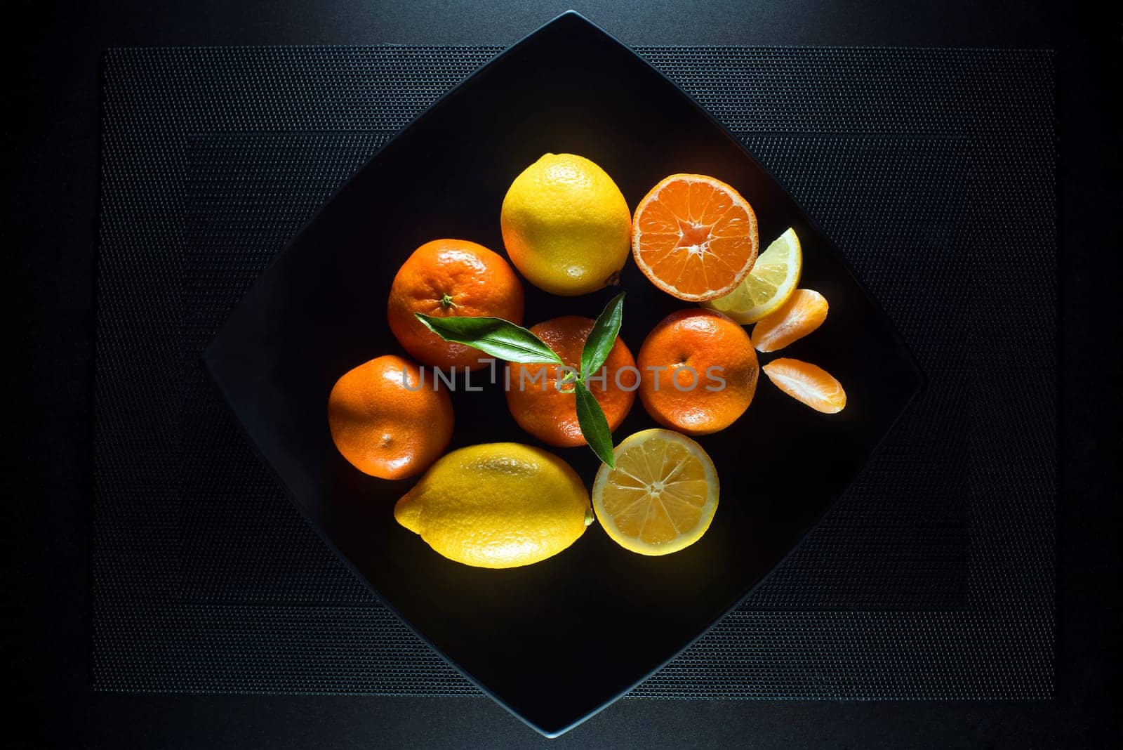 Ripe juicy tangerine, orange mandarin and lemon with leaves on black plate.