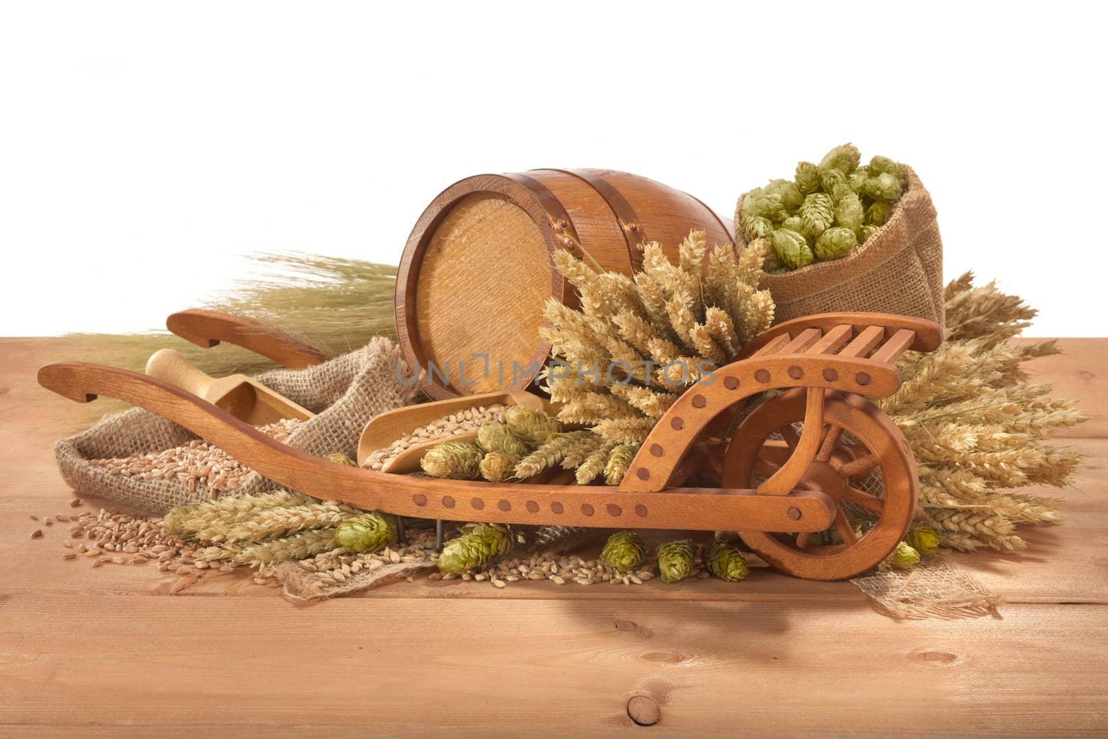 Old barrel with wheelbarrow,wheat,barley,hops and malt against a white background