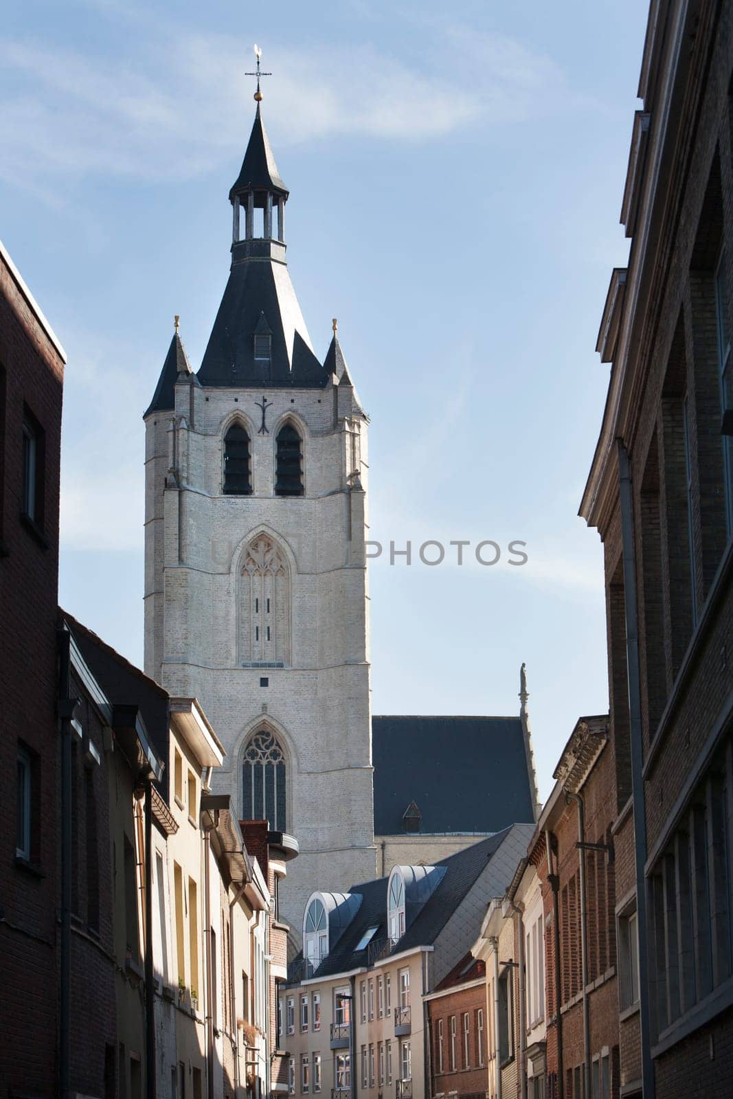 The Church of Our Lady across the river Dijle in Mechelen was founded in 1236. In Dutch language it's called the Onze-Lieve-Vrouwekerk. The sunlight in the street leads to the white Brabant gothic style church. It’s one of the touristic attractions in Mechelen.