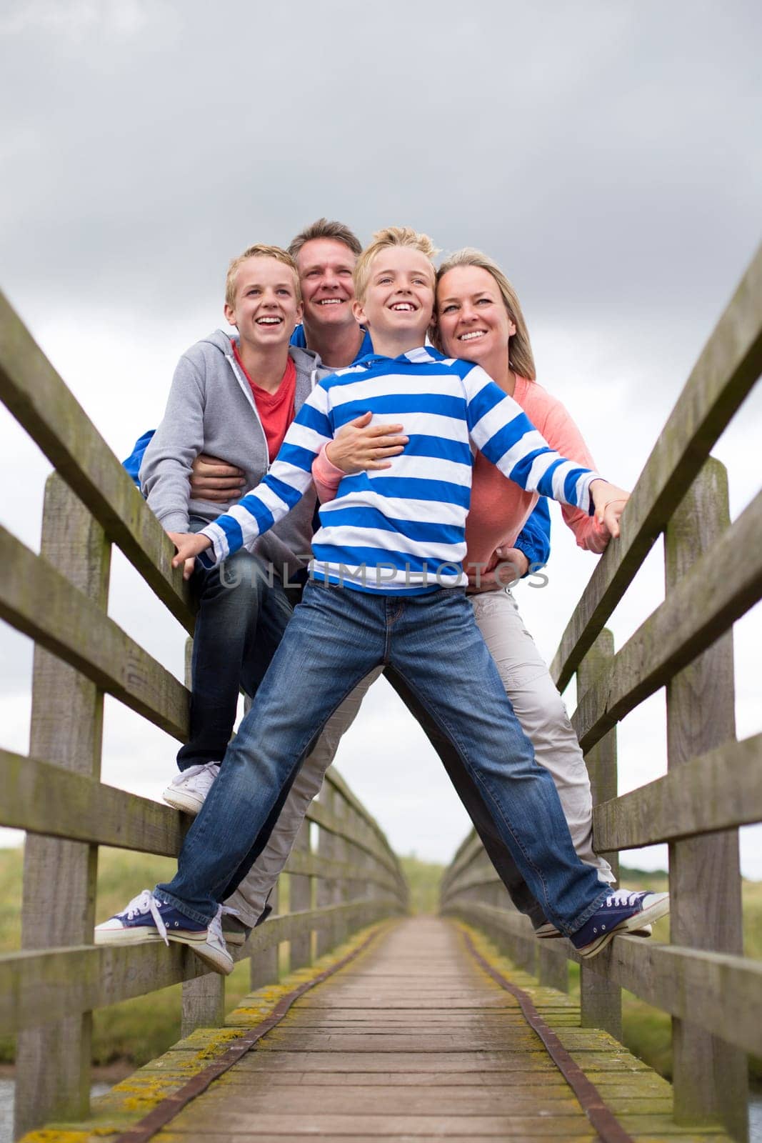 Family Portrait taken at a low angle on a bridge. They are wearing warm casual clothing and smiling.