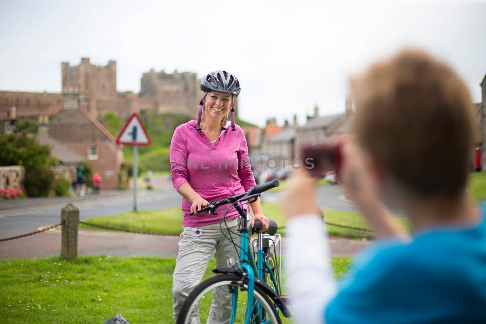 Mother posing for a picture on her bike. A village with a castle can be seen in the background, she is wearing a helmet and casual clothing.