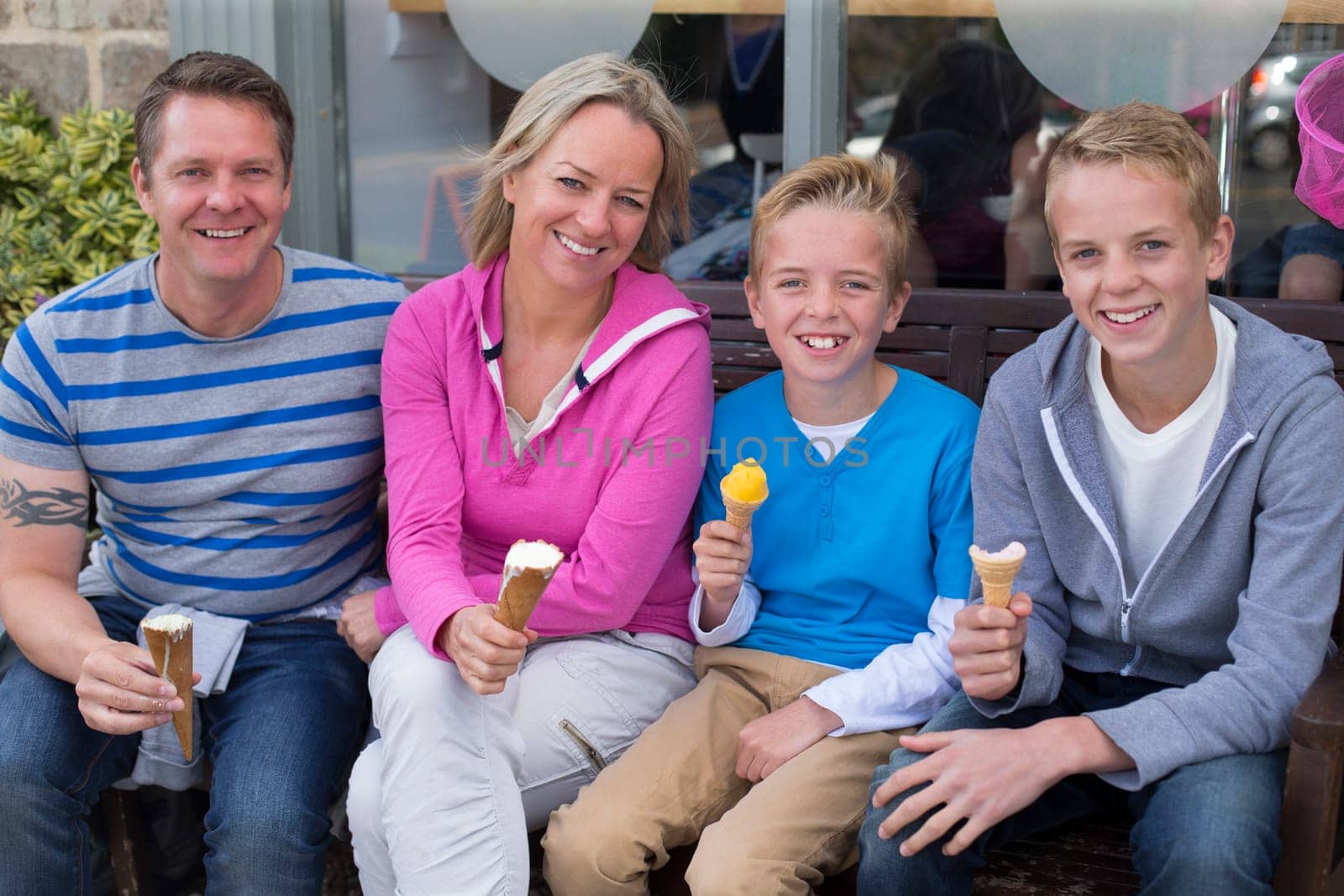Portrait of a family enjoying ice cream outside of a shop. They are wearing casual clothing and smiling at the camera.