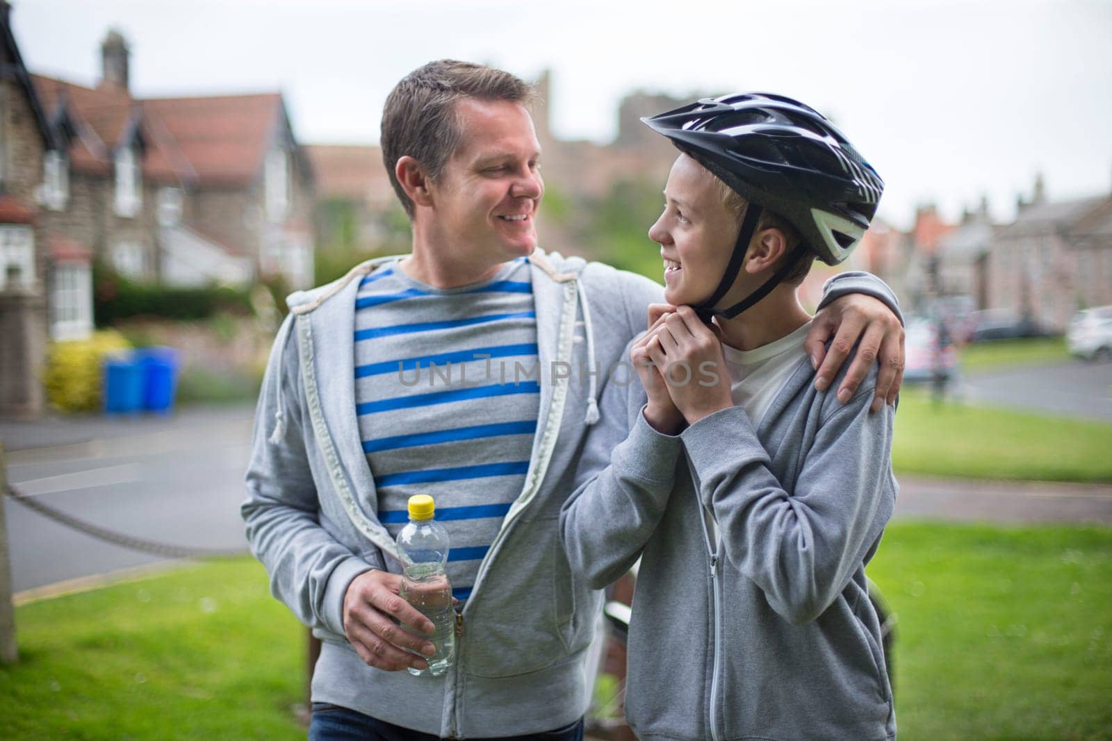 Father and Son getting ready for their bike ride. The father has his arm around his son and they are smiling at each other.