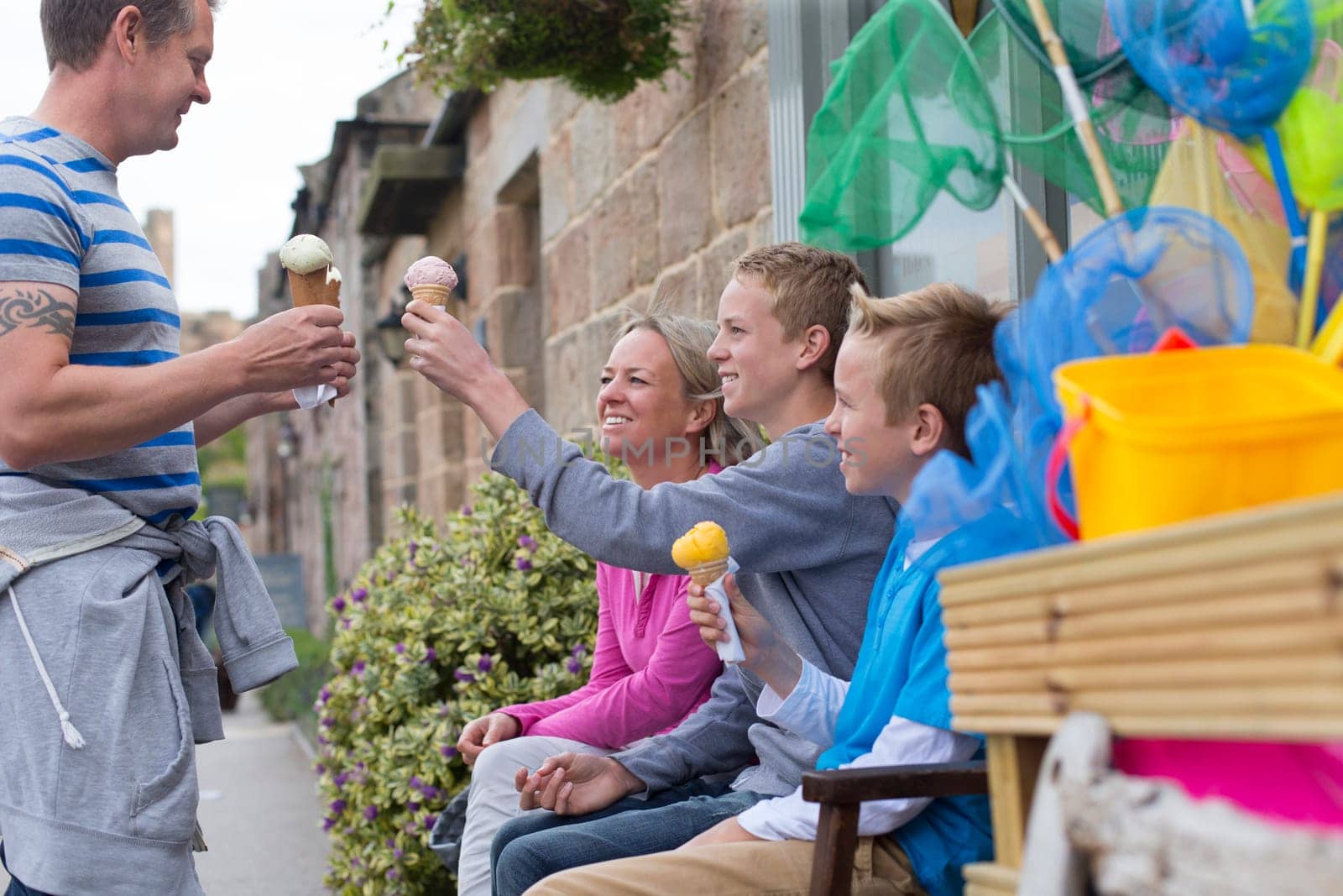 Family enjoying ice cream outside of a shop. They are all holding their cones and smiling.