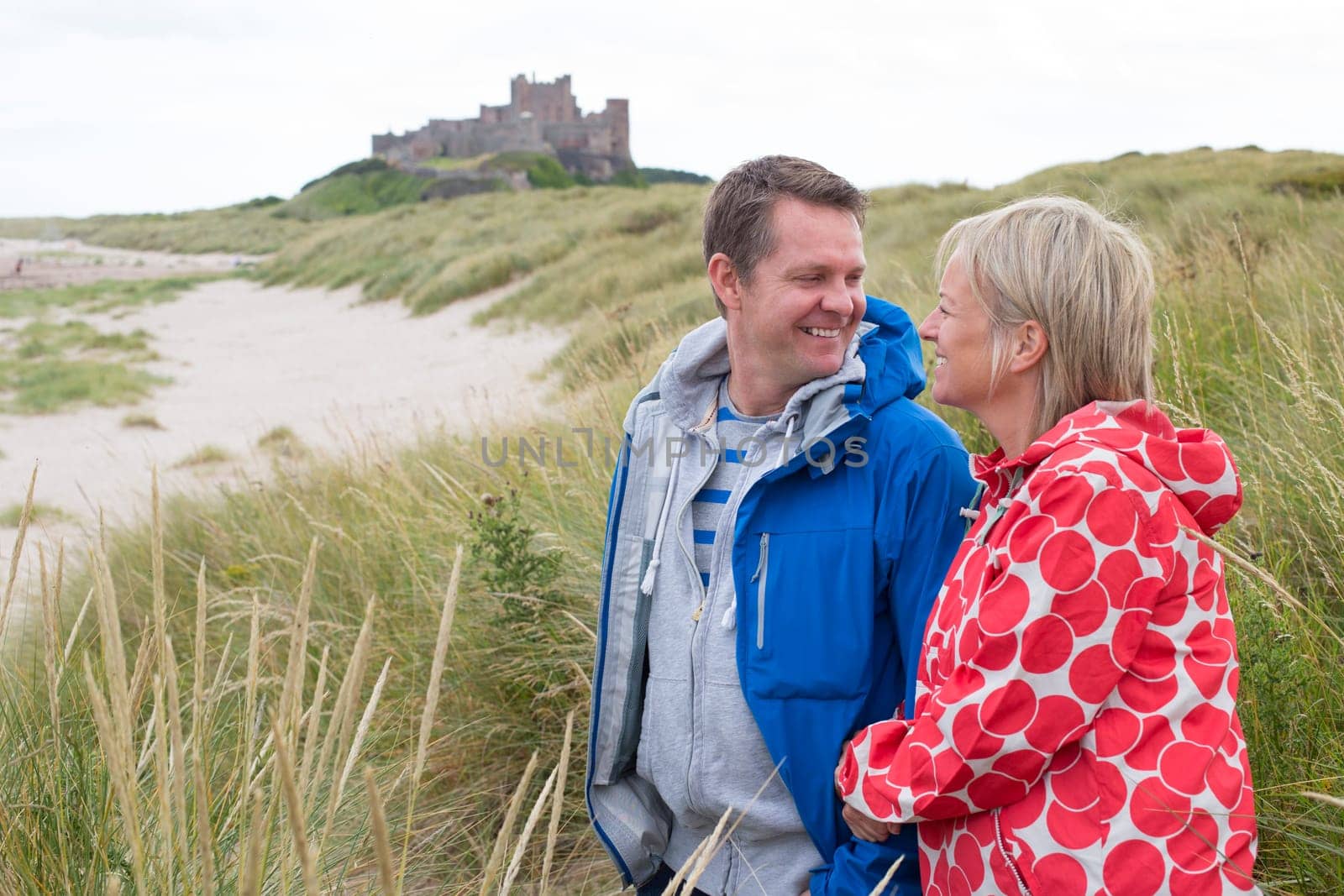 Happy Mature couple at the beach. They are wearing warm casual clothing and a castle can be seen in the distance in the background.