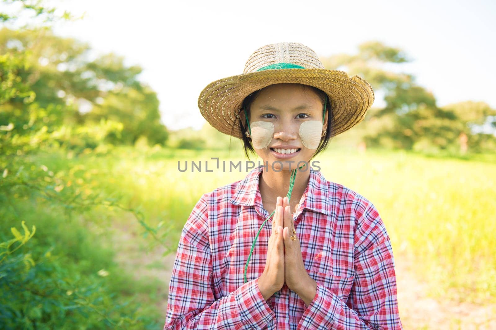 Portrait of a young Burmese female farmer with thanaka powdered face in blessing gesture.