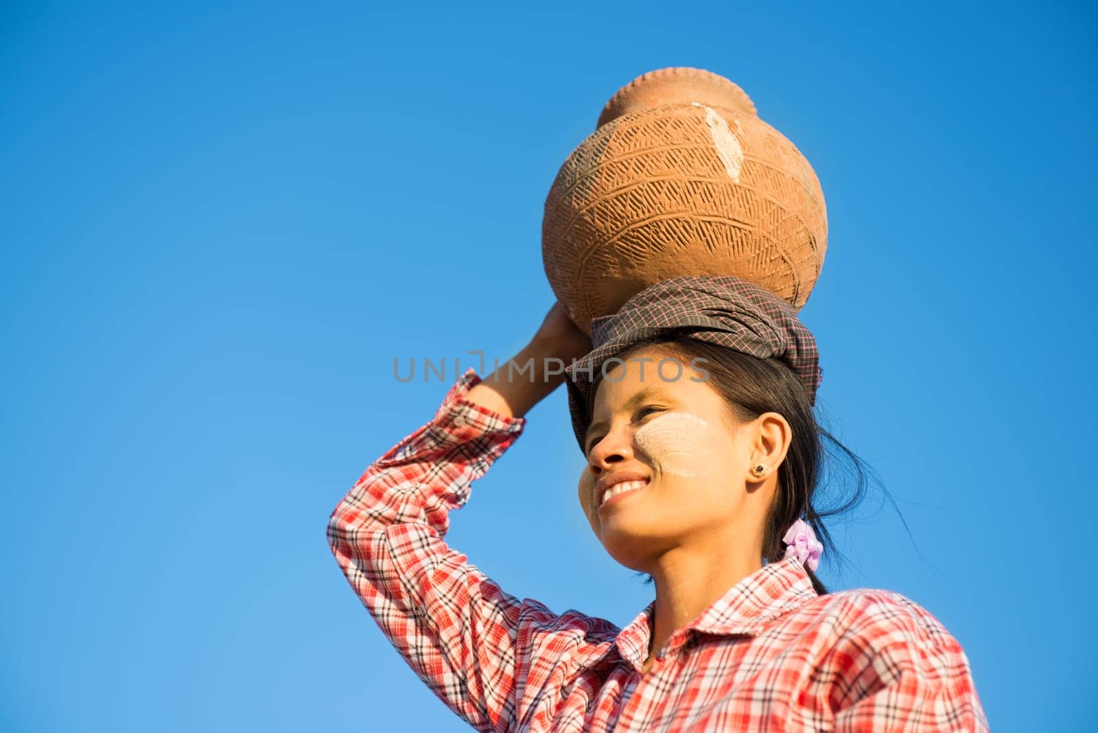 Portrait of Young Asian Burmese traditional female farmer carrying clay pot on head going back home, Bagan, Myanmar
