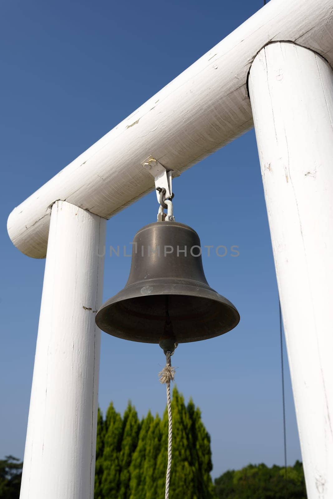 Bronze bell hanging on wooden pillar on a blue sky