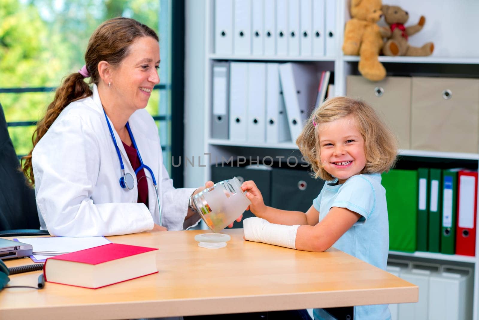 female pediatrician in white lab coat has candys for a little girl