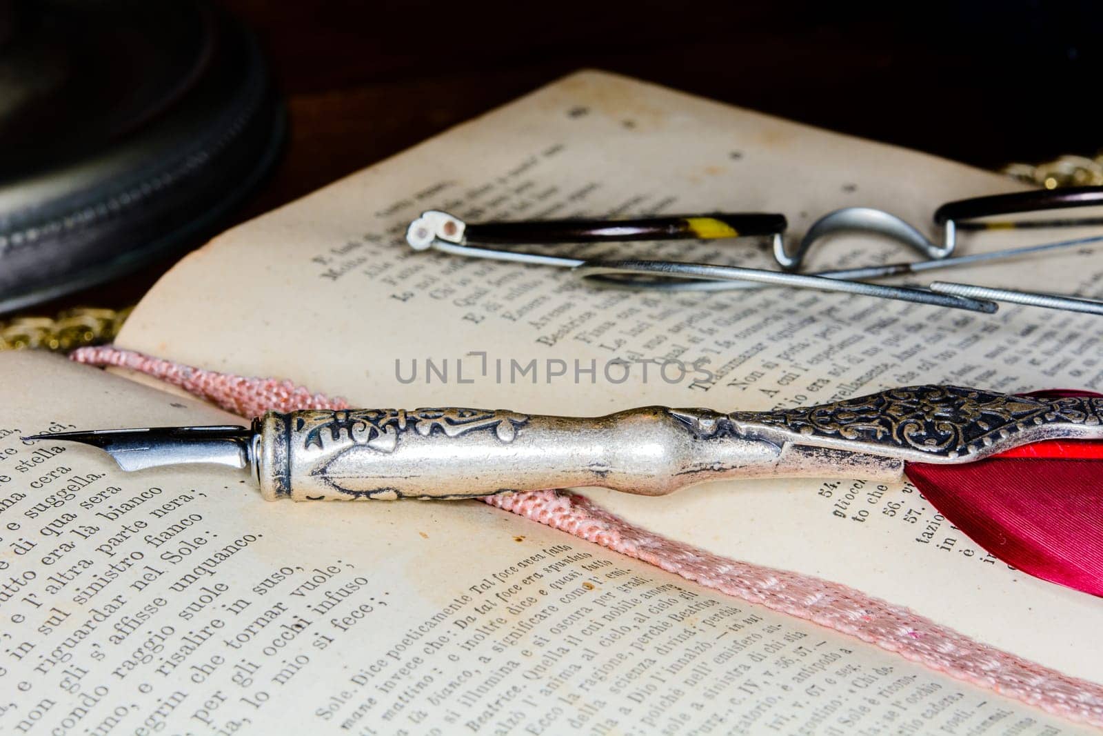 Ancient fountain pen over an old book - Dante's Divina Commedia, Italy version and glasses. Dark background in shadow.