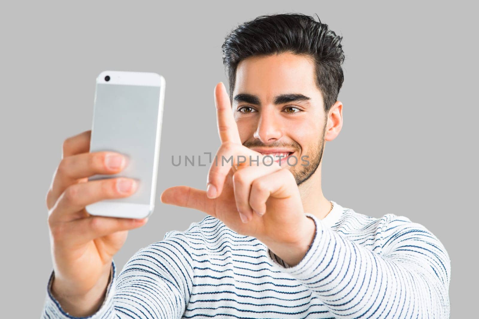Handsome young man making a selfie picture with phone, isolated over gray background