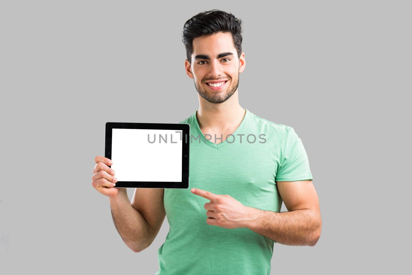 Handsome young man showing something on a tablet, isolated over gray background
