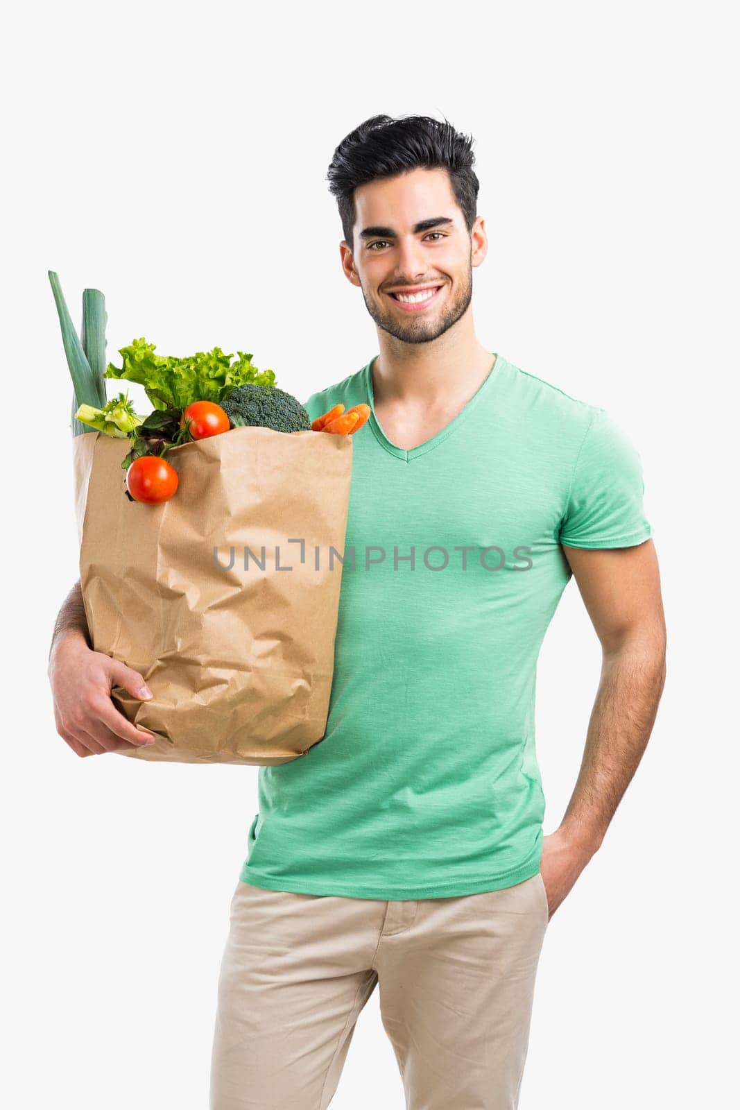 Handsome young man carrying a bag full of vegetables, isolated over gray background