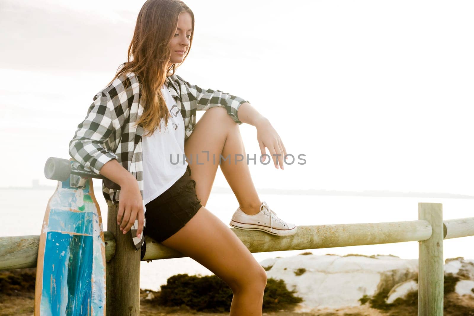 Beautiful and fashion young woman posing at the sunset with a skateboard