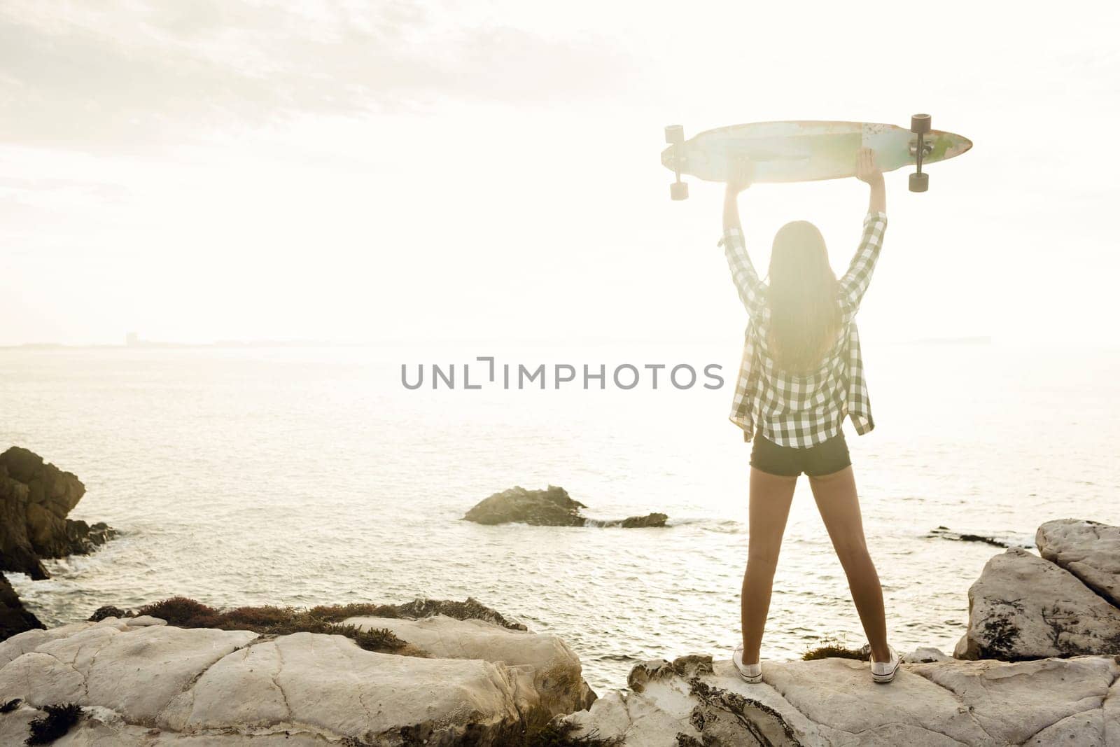 Beautiful and fashion young woman posing at the sunset with a skateboard