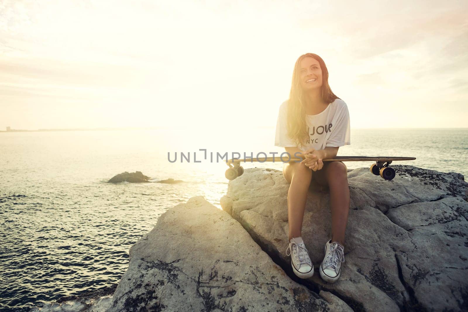 Beautiful and fashion young woman posing at the sunset with a skateboard