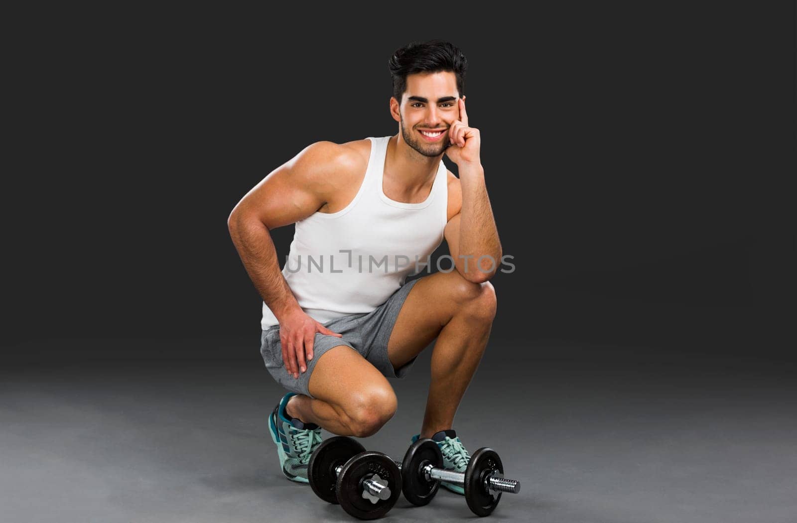 Portrait of handsome young man lifting weights, isolated over a gray background