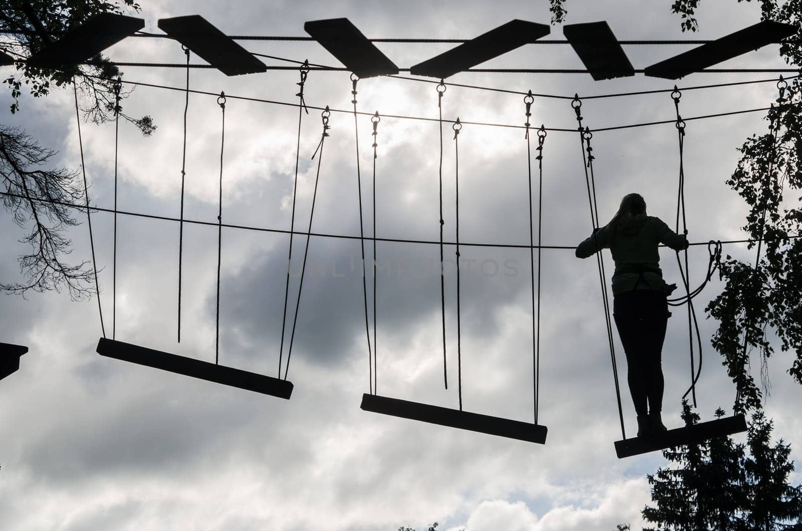 Silhouette of the girl on Dangerous ropeway with tether in rope park