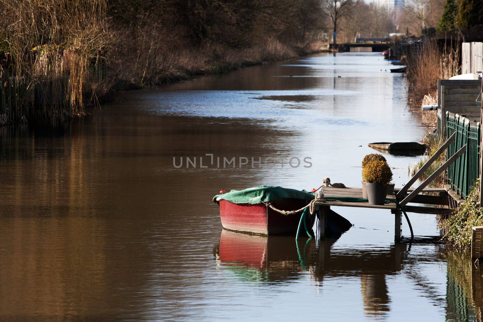 Tranquil and idyllic scene of a red boat with a green awning, moored with a rope, at a backyard jetty.