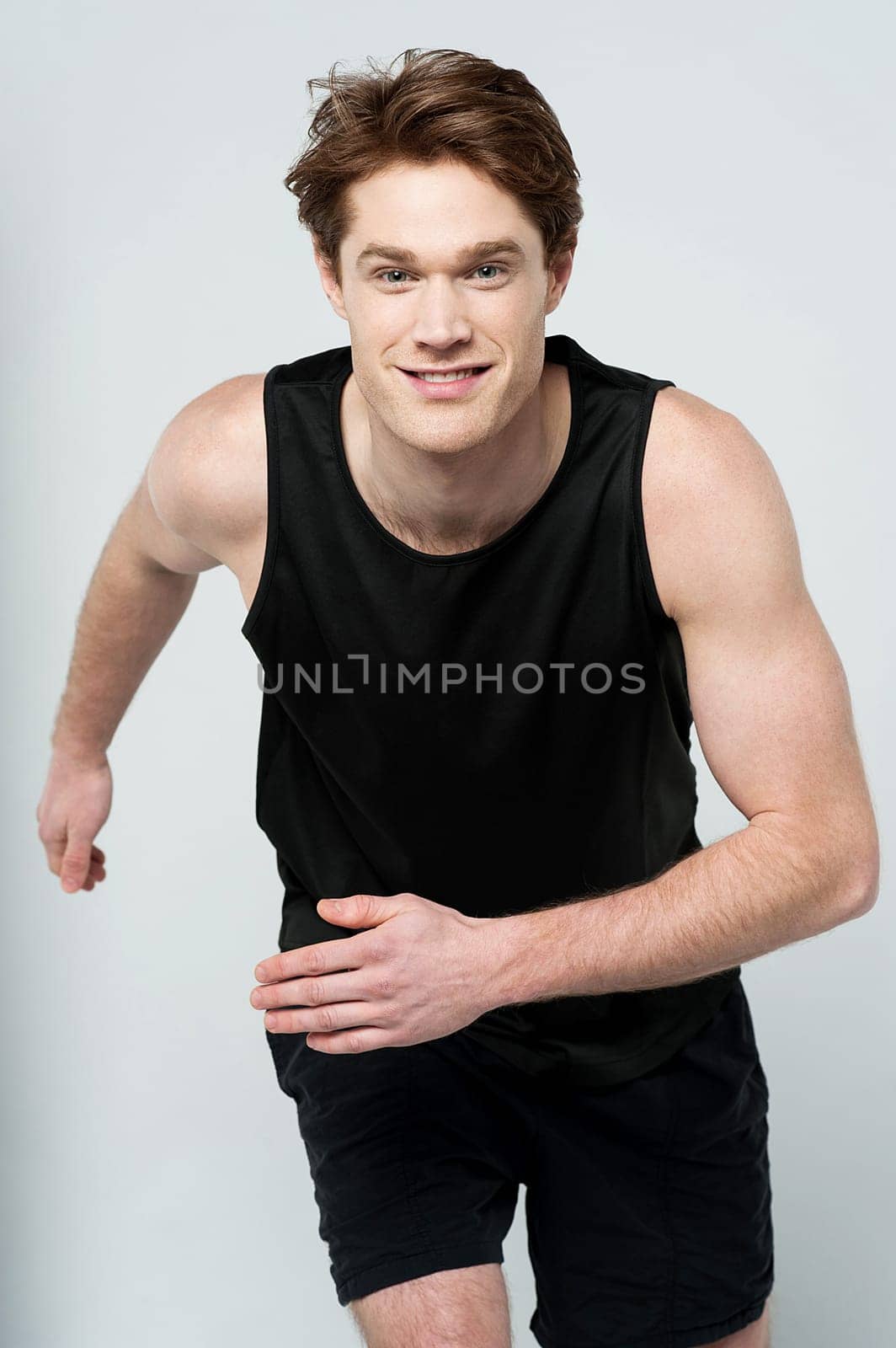 Young sports man running against grey background