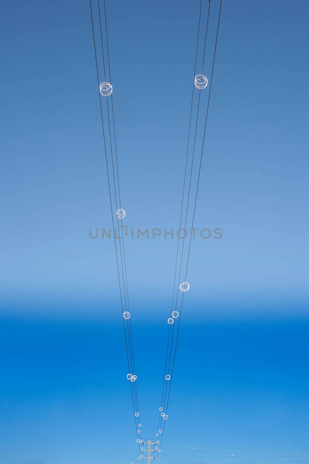 Power line wires over blue sky on vertical perspective. Closeup