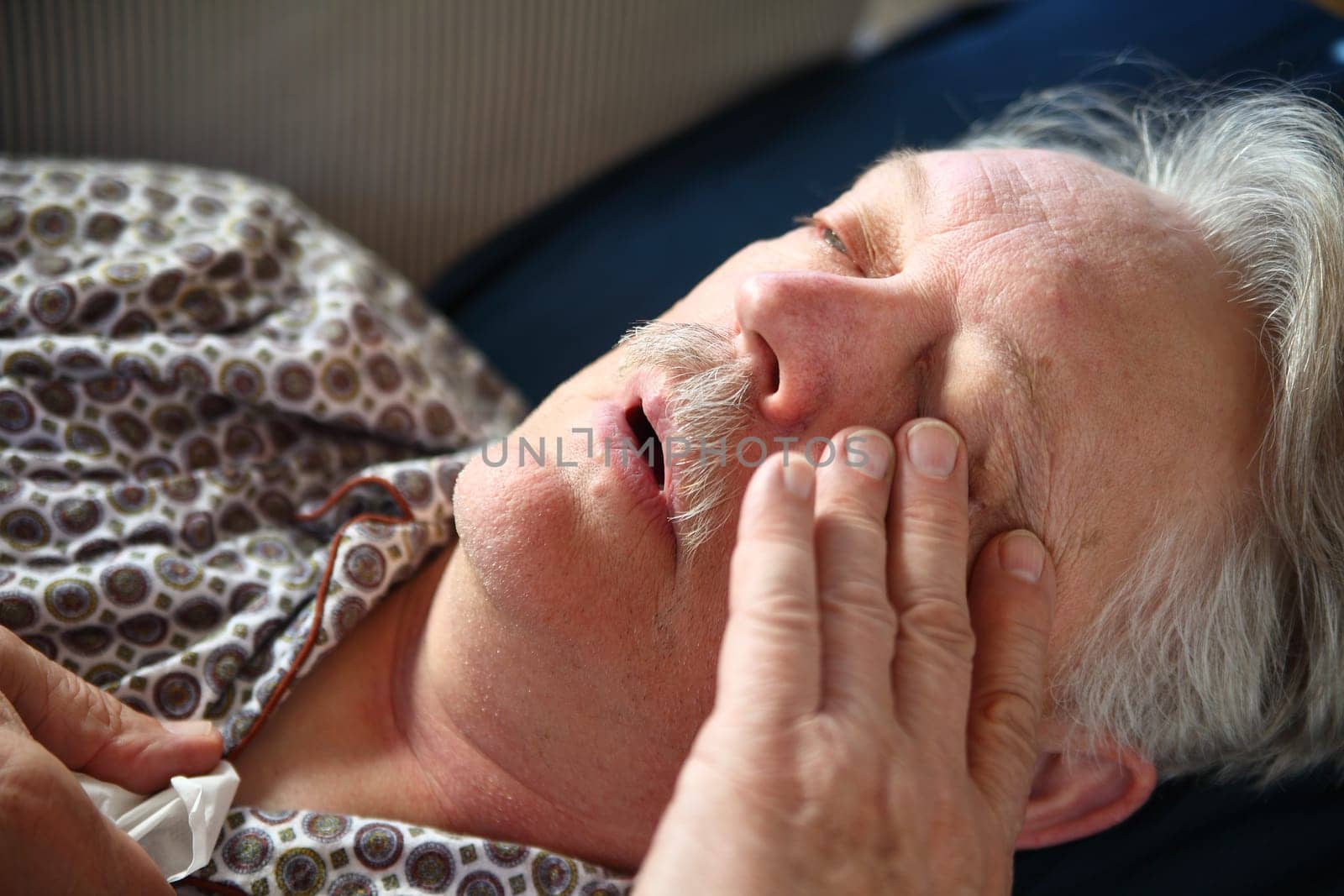 A senior man suffers the miseries of the flu while lying on a sofa.