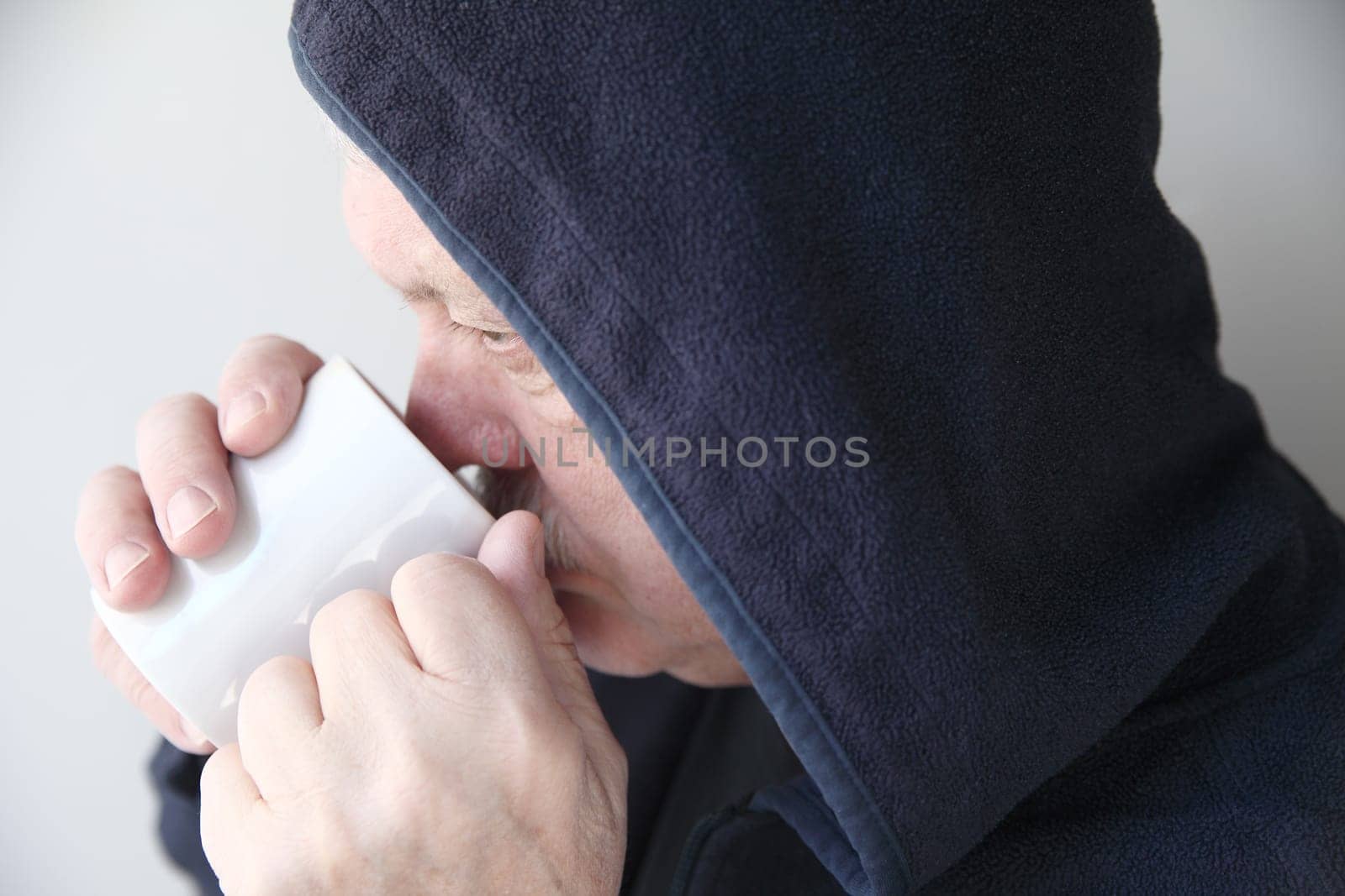 Older man wearing a black hoodie drinks his morning coffee.